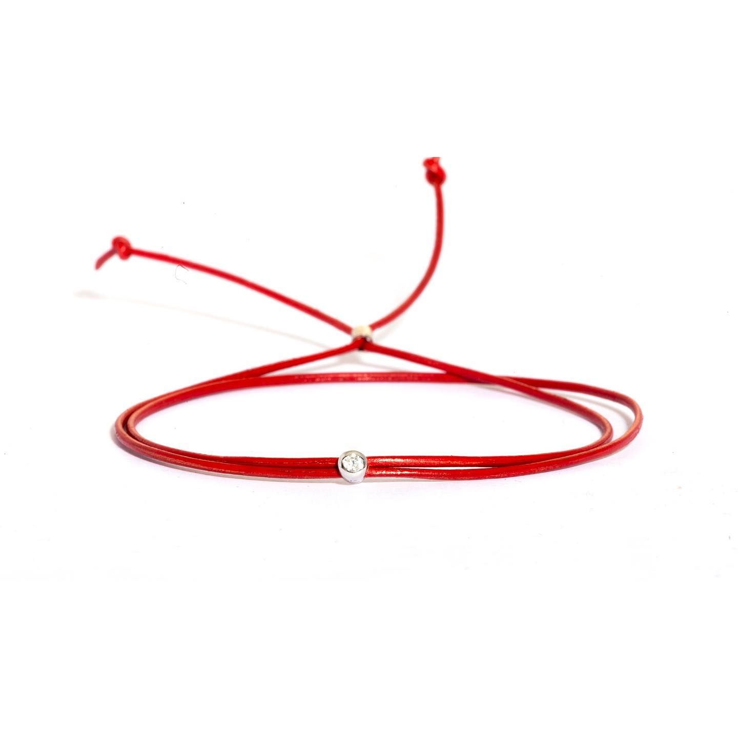 Bracelet cordon rouge avec une petite breloque argentée, réglable par un noeud coulissant.