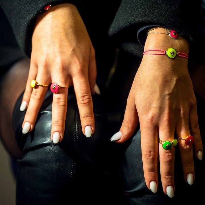 Mains de femme avec bagues et bracelet assortis, chacun avec des motifs de fleurs circulaires colorées, sur cuir noir.