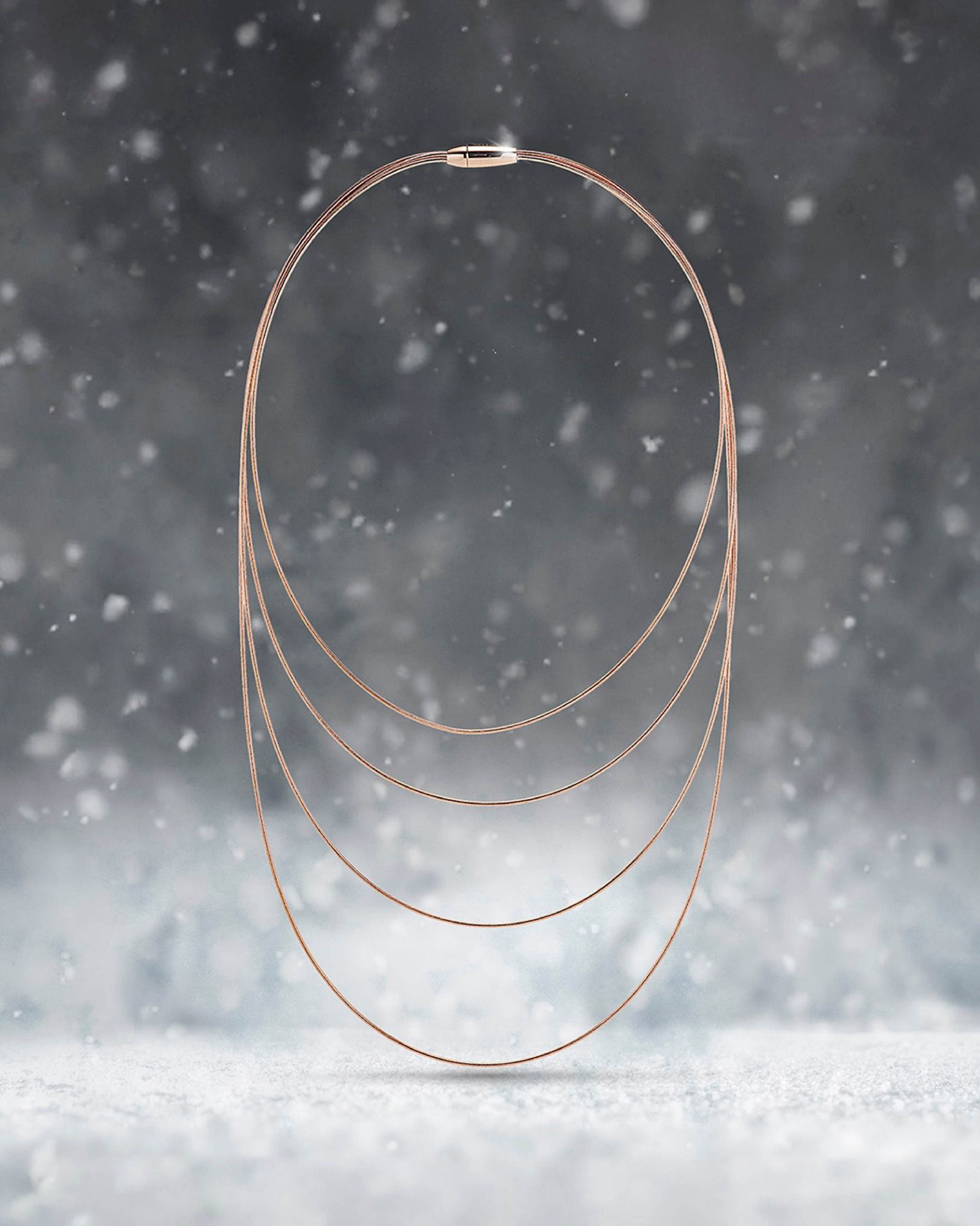 Collier superposé en or rose sur un fond enneigé et flou.