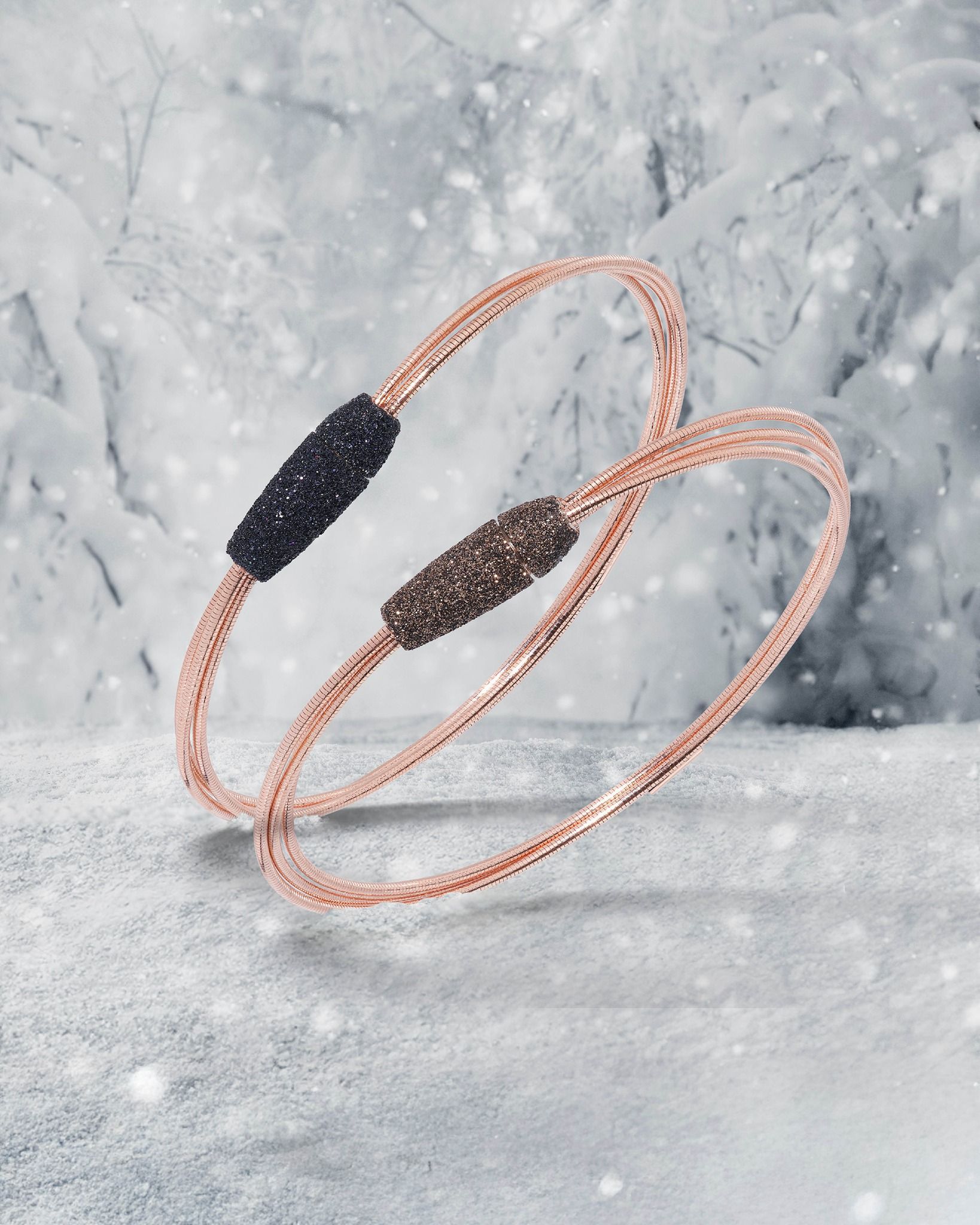 Deux bracelets en or rose avec des détails centraux en perles sur un fond enneigé.