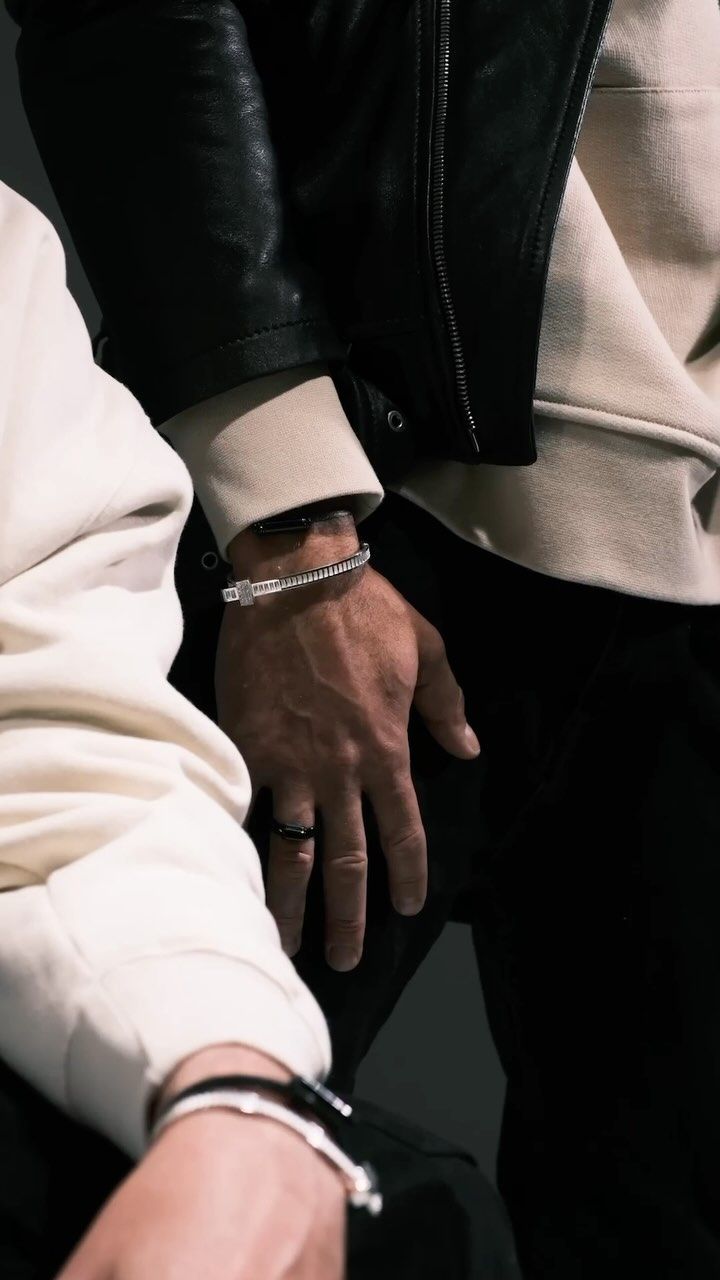 Deux personnes, gros plan : mains et bras portant des bracelets et des bagues, l'une en veste de cuir et sweat à capuche.