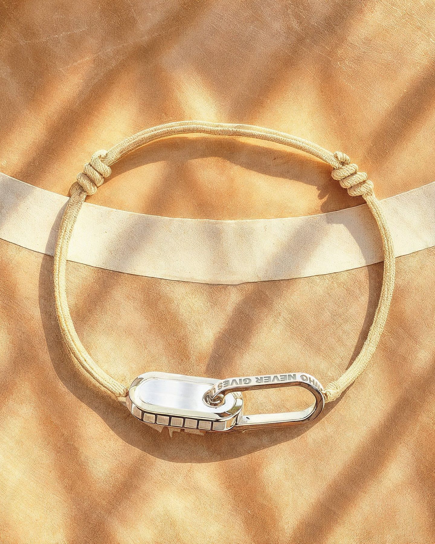 Bracelet en corde beige avec fermoir en argent sur une surface beige texturée.