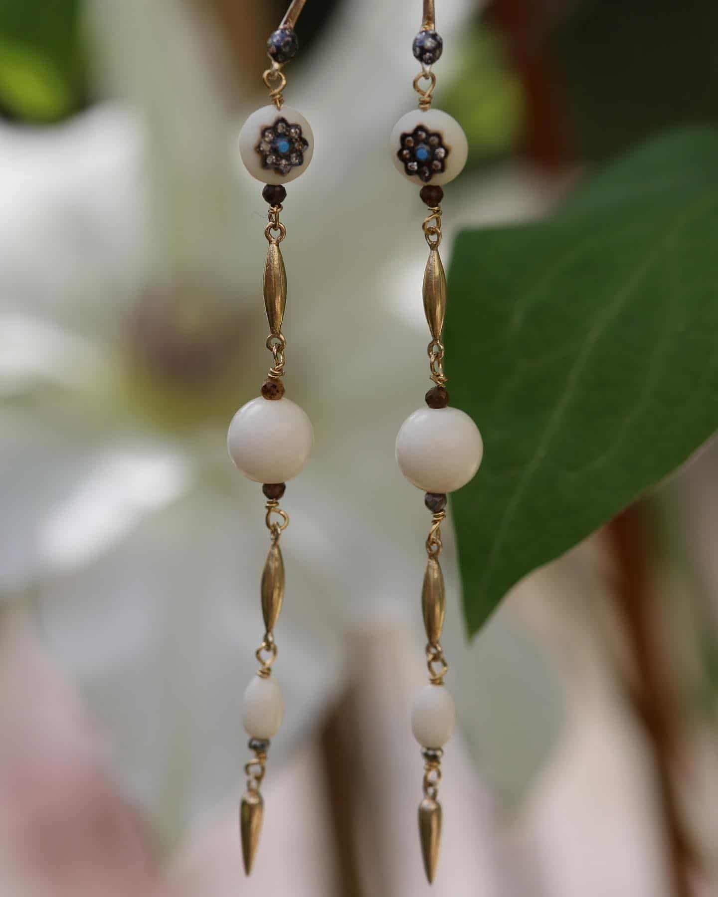 Boucles d'oreilles pendantes en or avec perles blanches, accents sombres et pointes pointues.