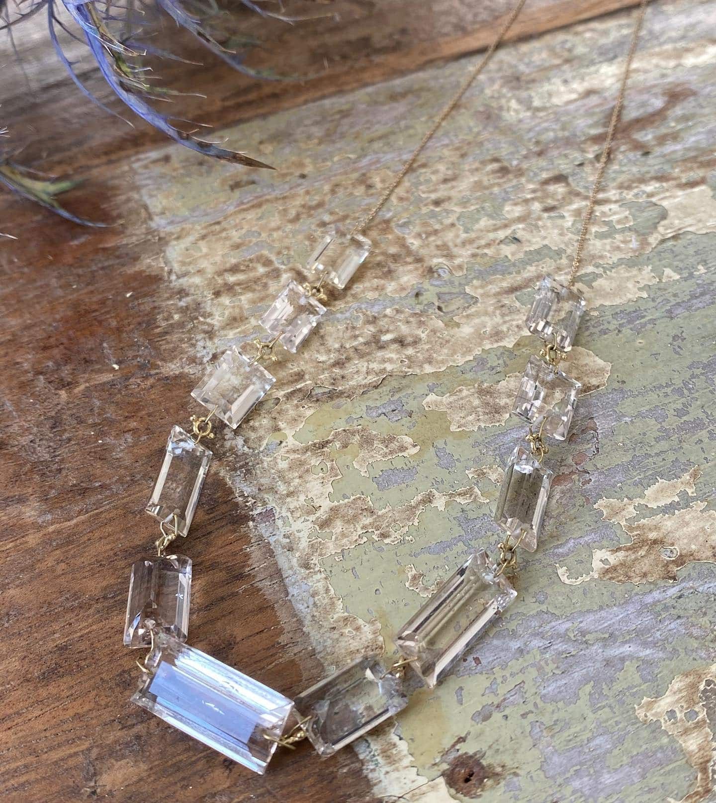 Collier délicat avec des perles rectangulaires transparentes sur une chaîne dorée, reposant sur une surface patinée et écaillée de peinture.