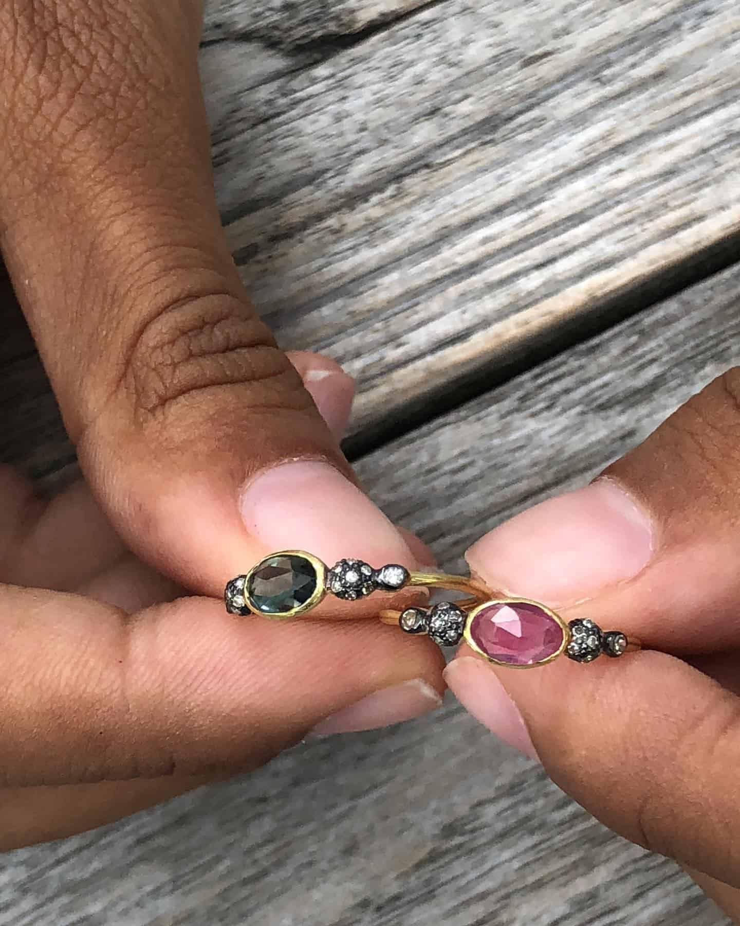 Personne tenant deux bagues en or avec des pierres colorées et de petits diamants.