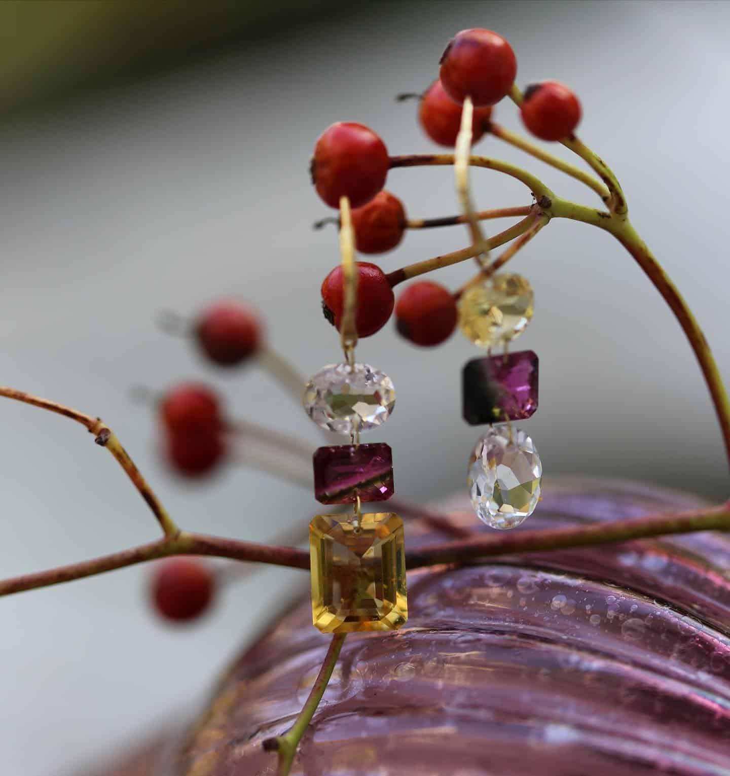 Boucles d'oreilles en or avec pierres précieuses colorées disposées sur une branche à baies rouges.