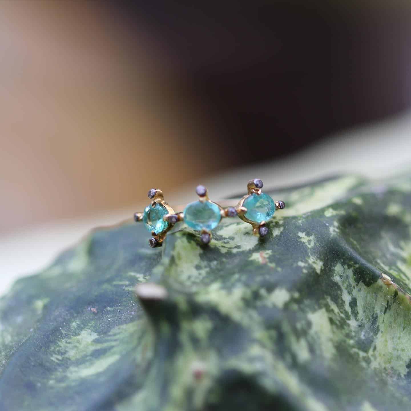 Bijou en or avec trois pierres turquoises reposant sur une feuille verte.
