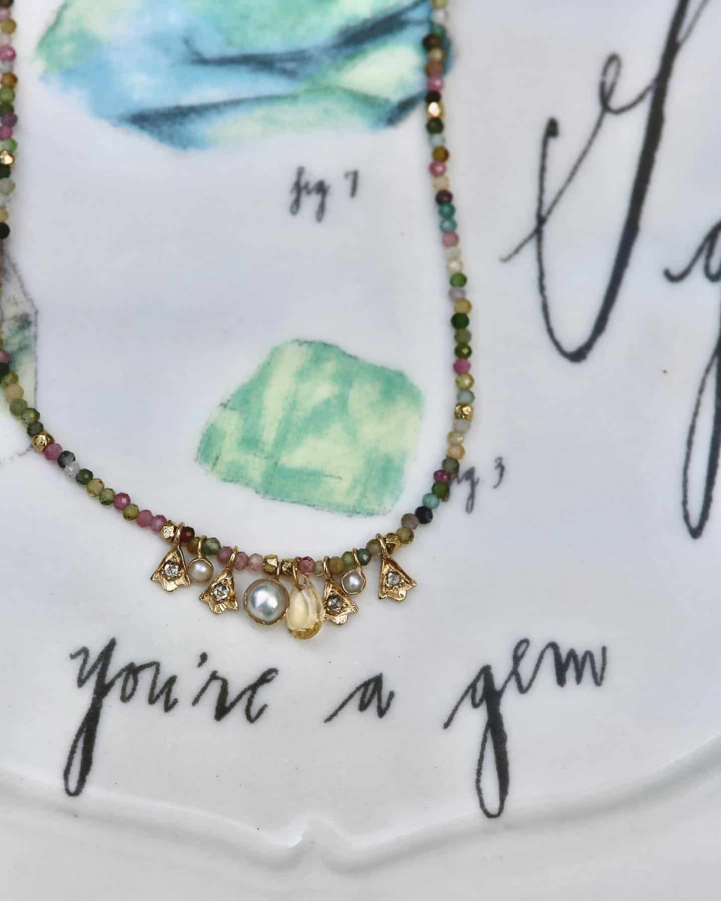 Collier avec perles multicolores, perles et breloques sur un tissu avec le texte « tu es un bijou ».