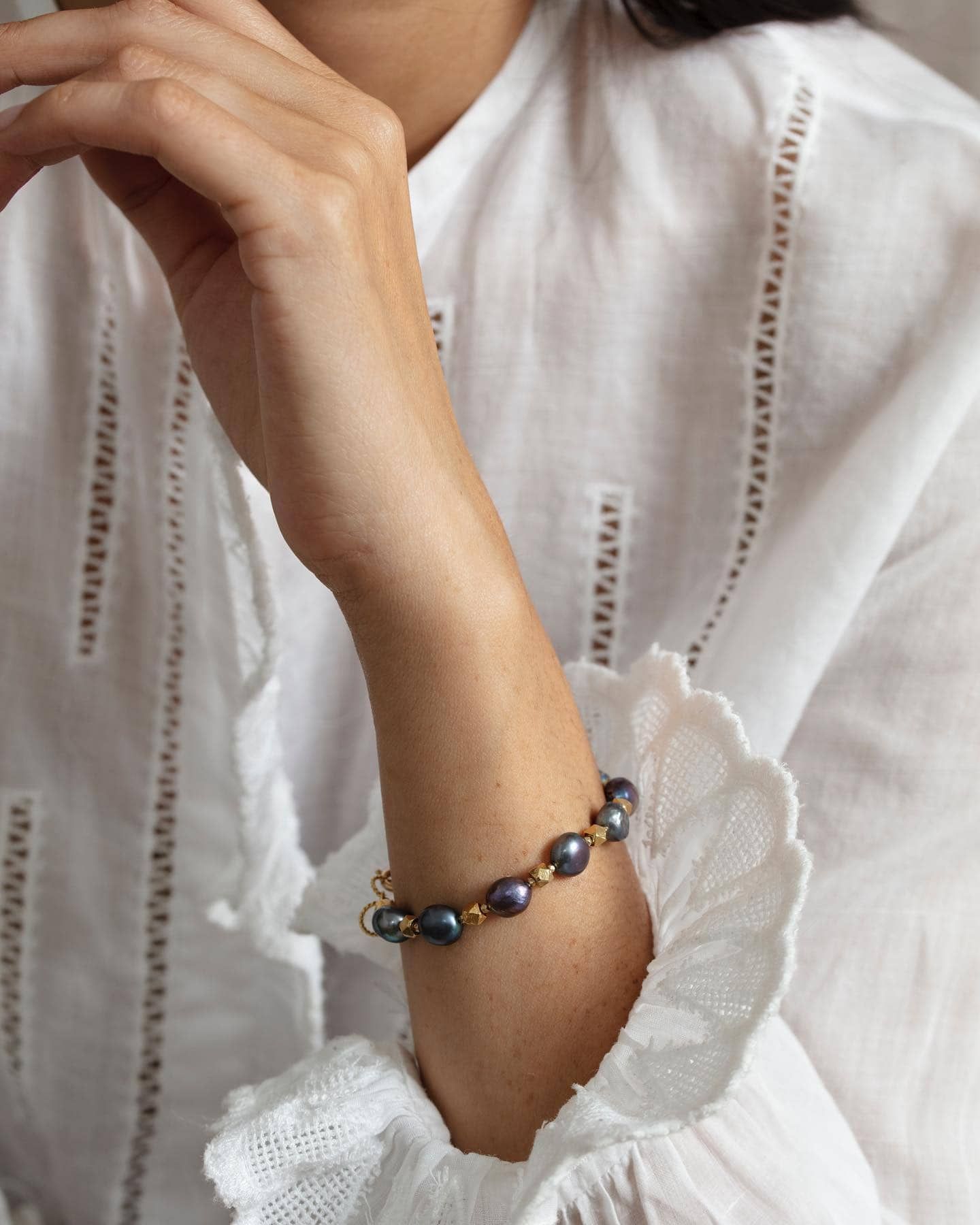 Bras d'une femme portant un bracelet de perles noires avec un fermoir en or et des perles d'accent ; posé sur un chemisier blanc.