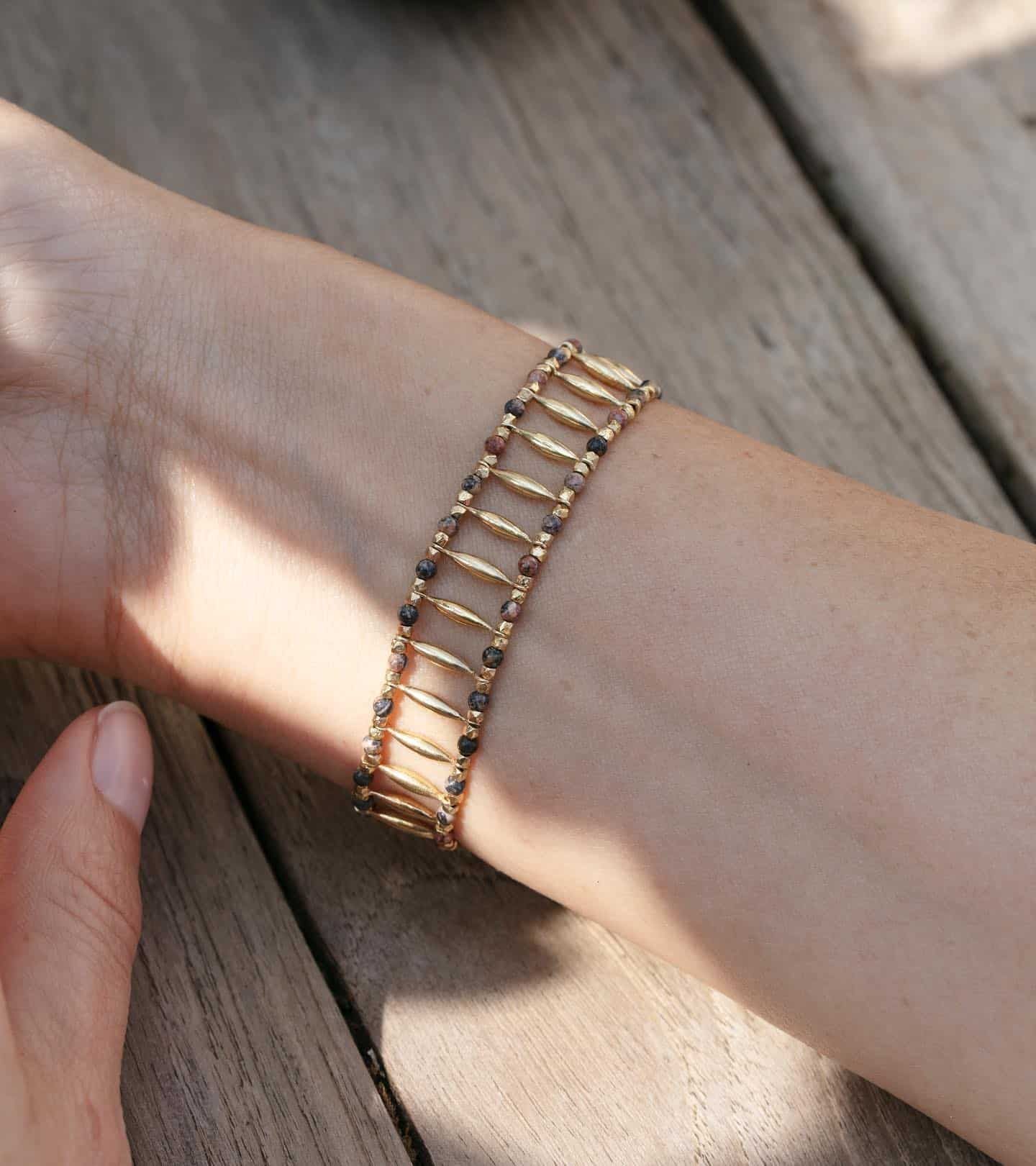 Bracelet en or avec des perles brunes sur le poignet d'une personne, posé sur une surface en bois.