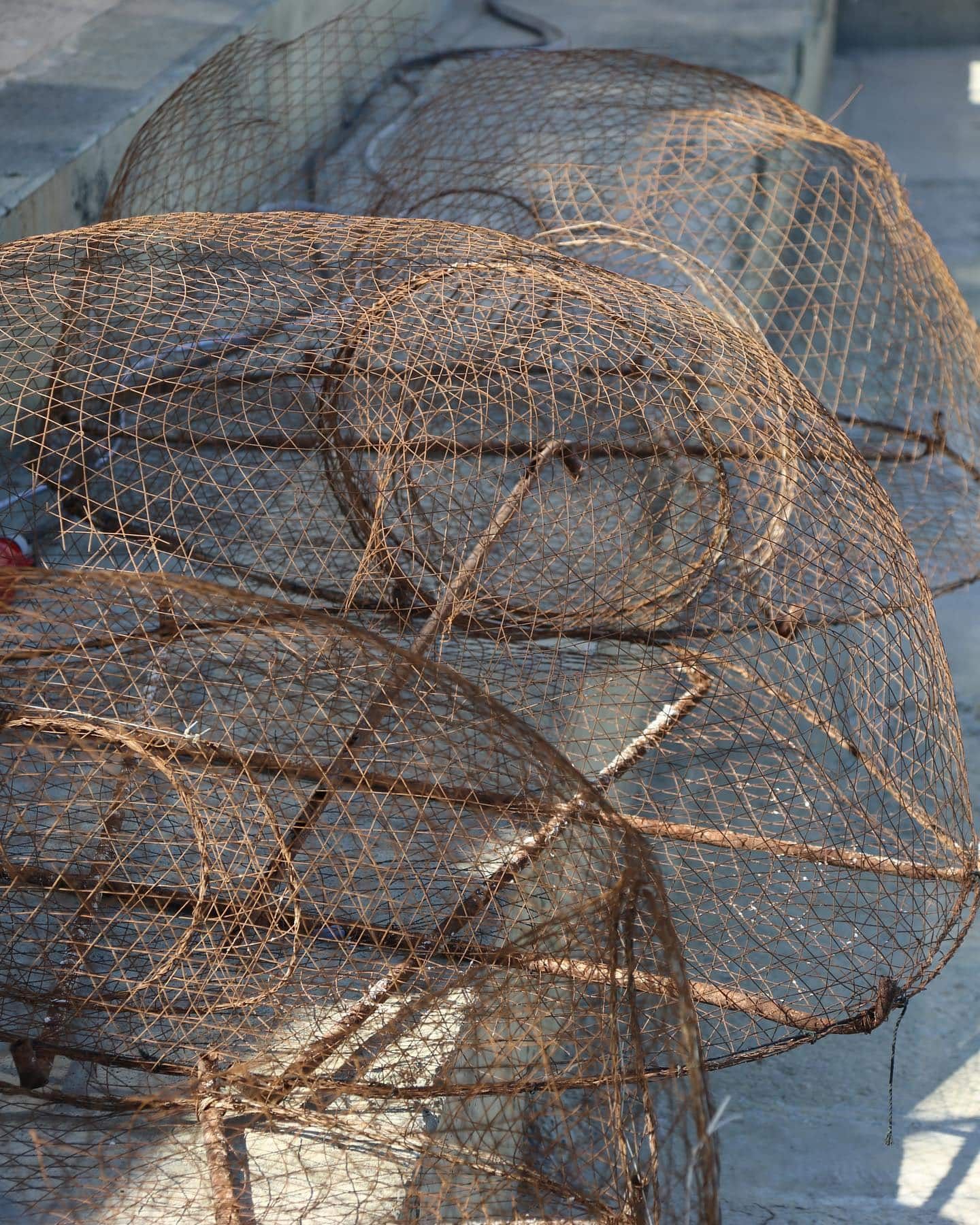 Pièges à crabes en fil de fer rouillé empilés sur une surface en béton, probablement près d'un quai.