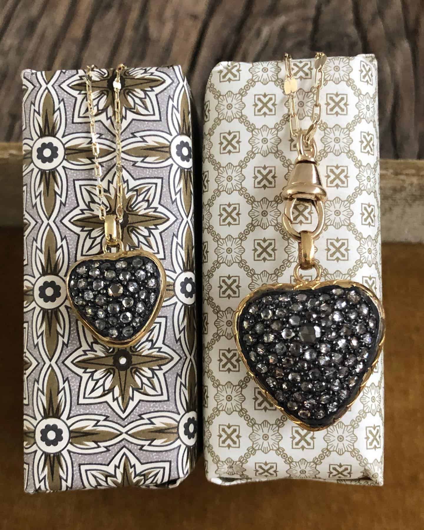 Deux colliers pendentifs en forme de cœur sur papier cadeau à motifs ; pierres dorées et noires.