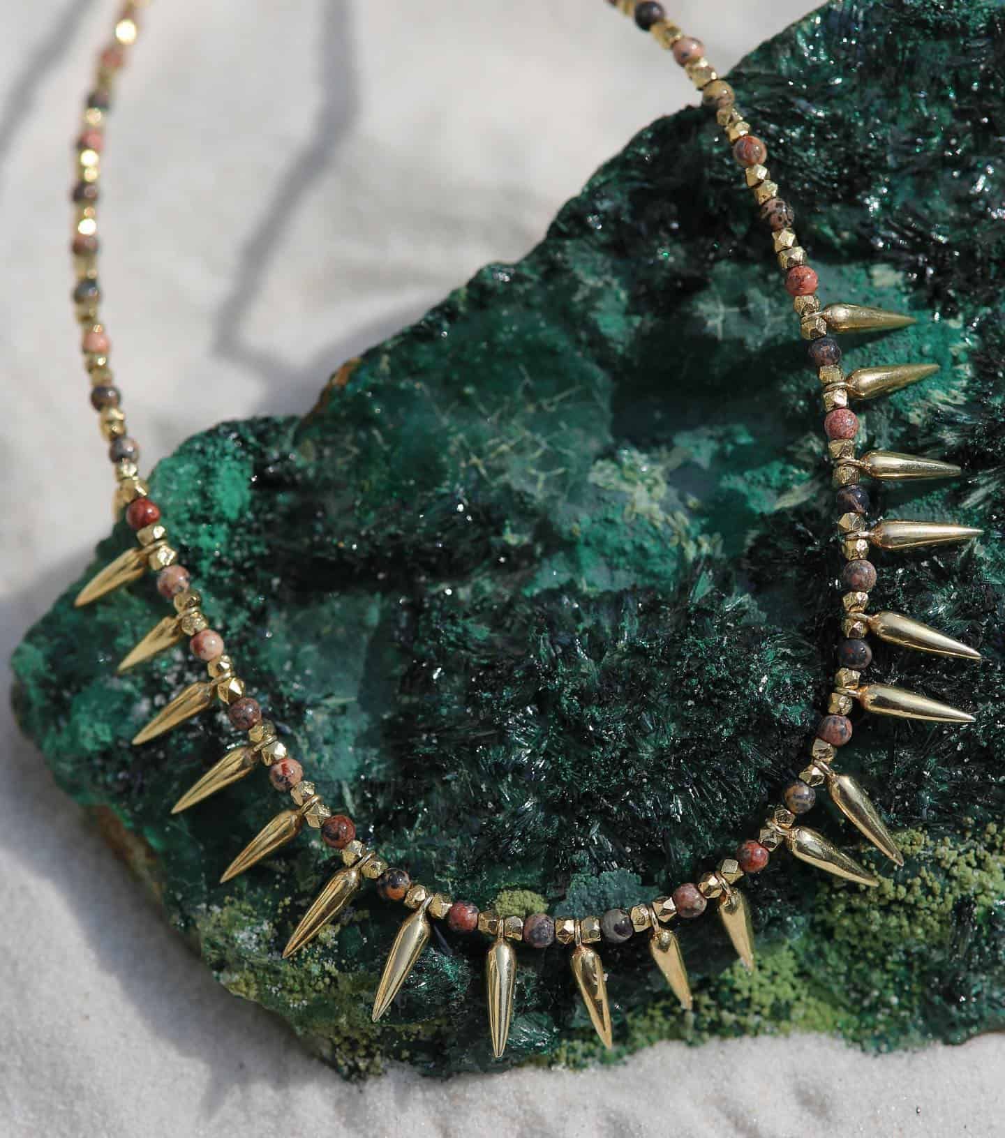 Collier à pointes en or sur une pierre verte à la texture rugueuse. Chaîne perlée multicolore.