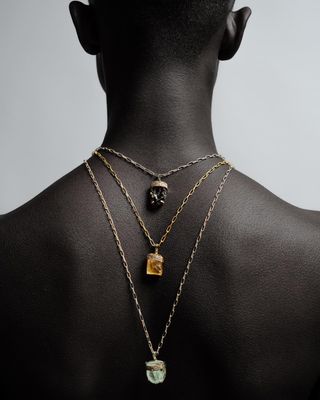 Le dos d'une personne noire avec trois colliers en or, chacun avec une pierre précieuse différente.