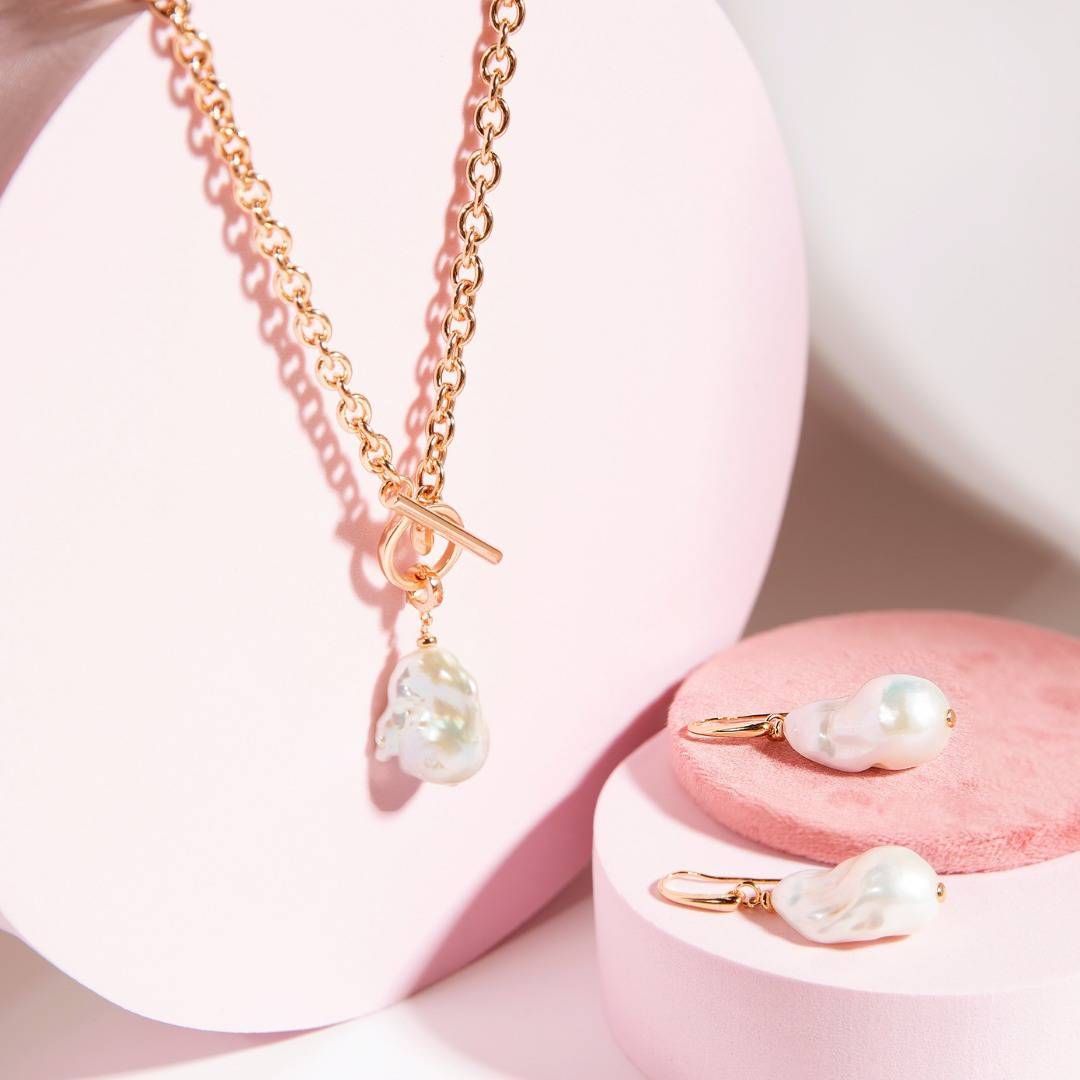 Collier en or avec un pendentif en perle et des boucles d'oreilles en perles assorties sur des blocs de présentation roses.