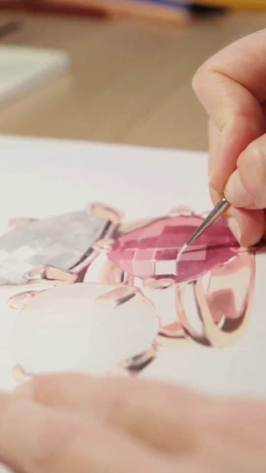Une main utilisant un outil pour affiner la couleur rose dans le dessin d'un bijou.