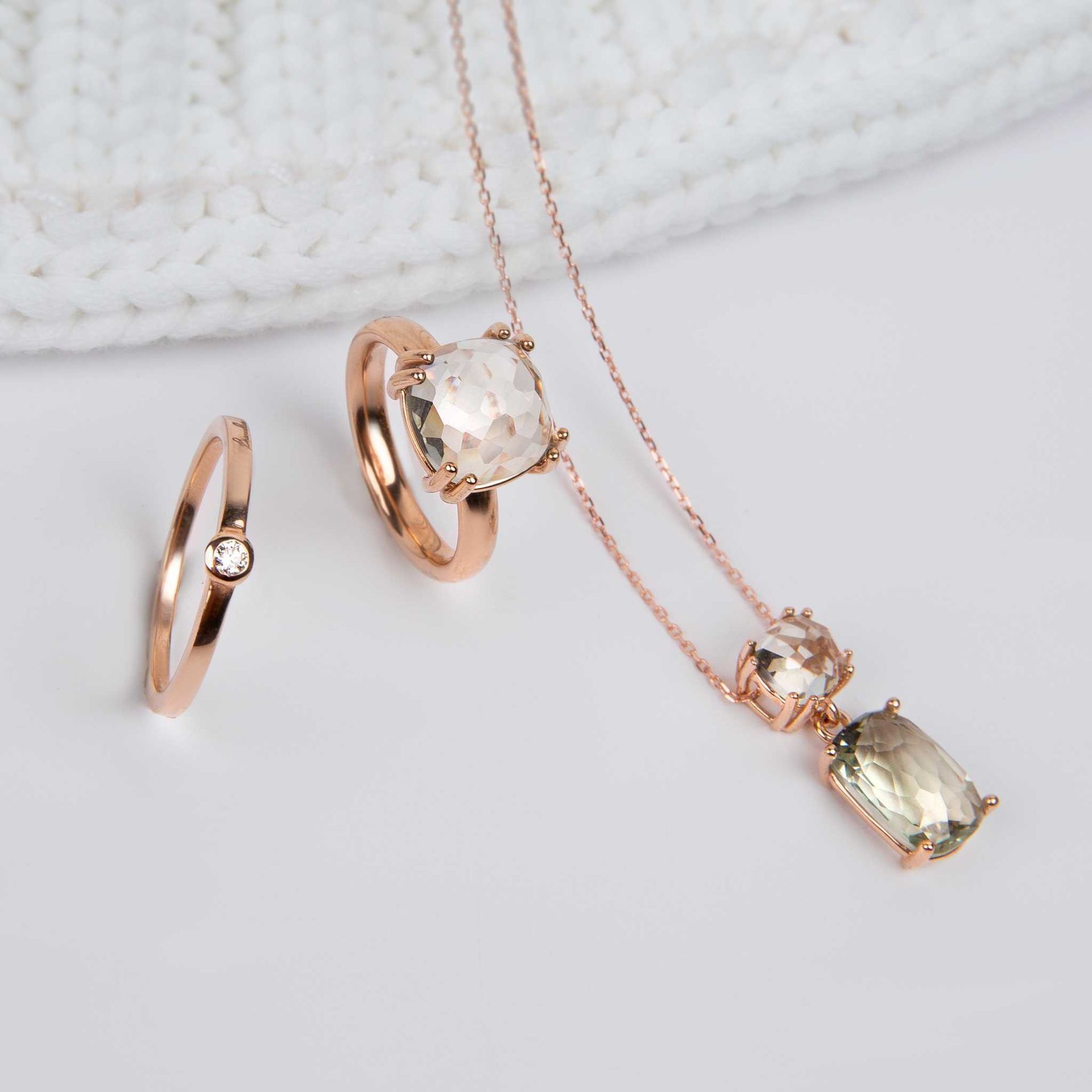 Trois pièces de bijoux en or rose avec des pierres vert clair sur fond blanc : un collier et deux bagues.