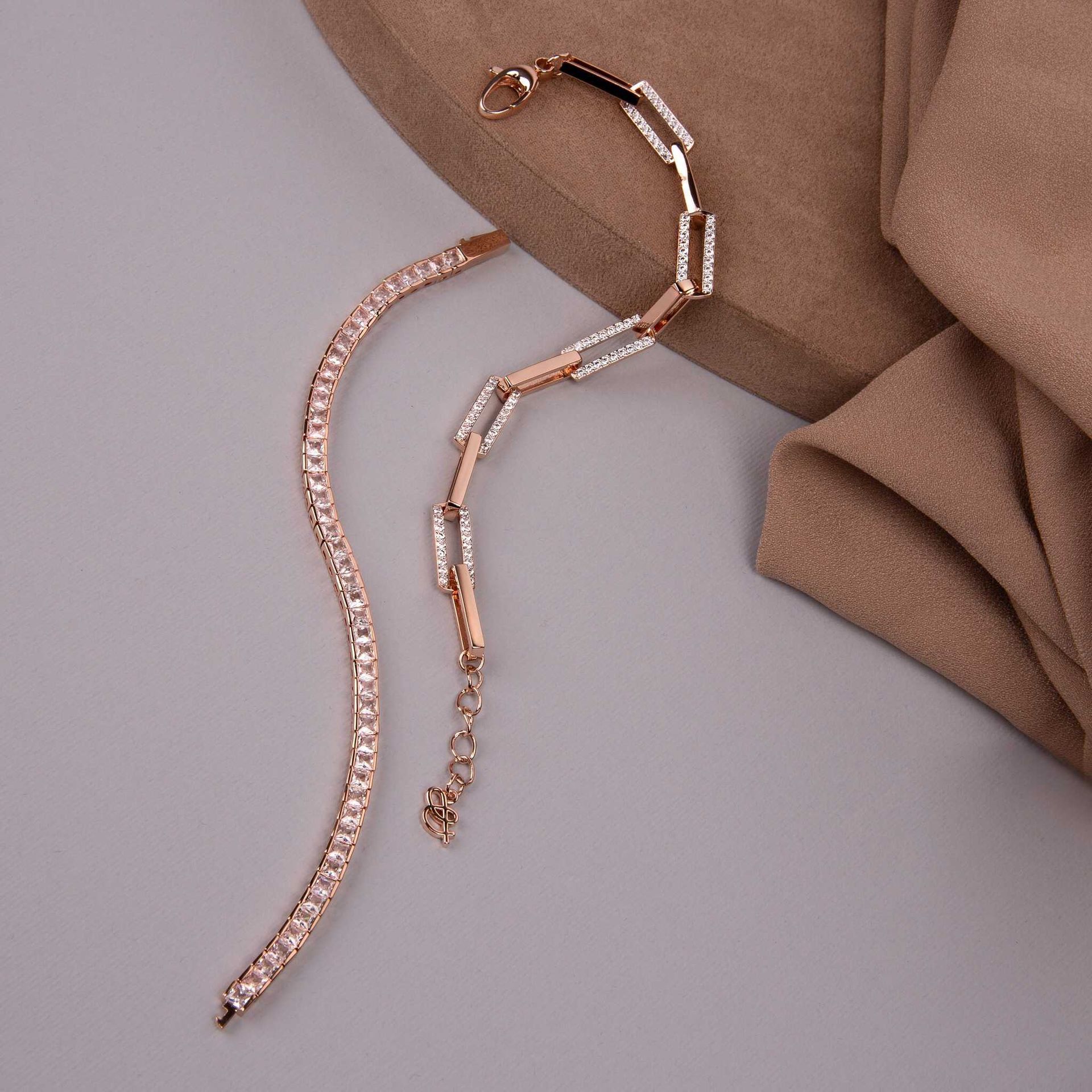 Deux bracelets en or rose avec des détails scintillants sur un fond neutre.