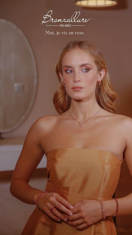 Femme portant des bijoux, debout à l'intérieur, dans une robe dorée, regardant sur le côté.