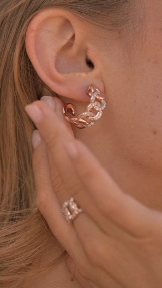 Boucle d'oreille créole femme avec chaîne en or rose, main touchant le visage, bague assortie.