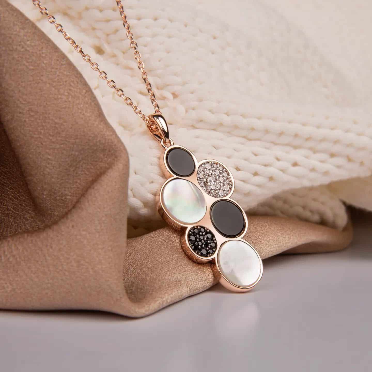 Collier en or rose avec un pendentif composé de cercles noirs, blancs et sertis de cristaux.