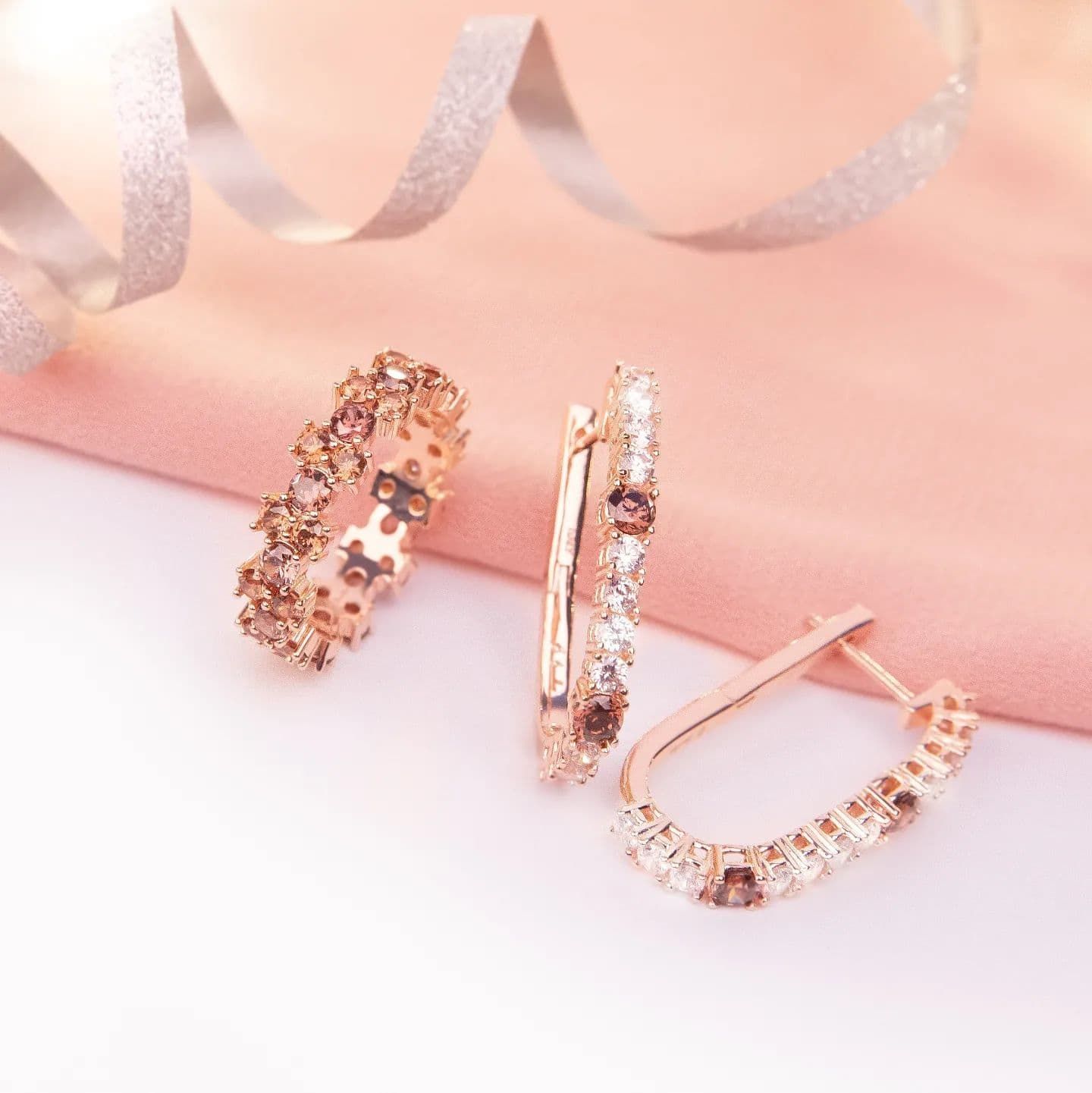 Boucles d'oreilles et bague en or rose avec pierres brunes et claires sur tissu rose.