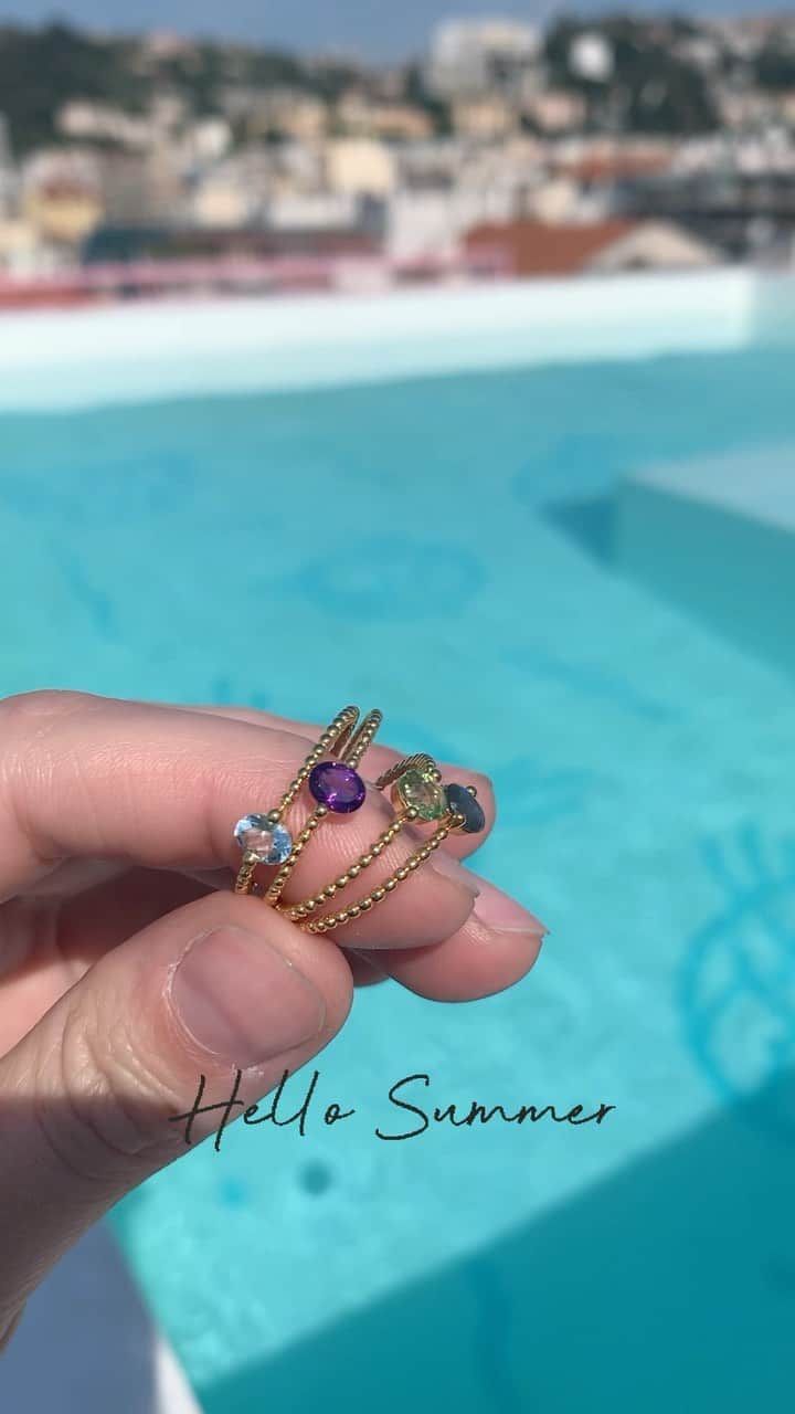 Main tenant trois bagues en or serties de pierres précieuses colorées, devant une piscine. Texte « Bonjour l'été » superposé.
