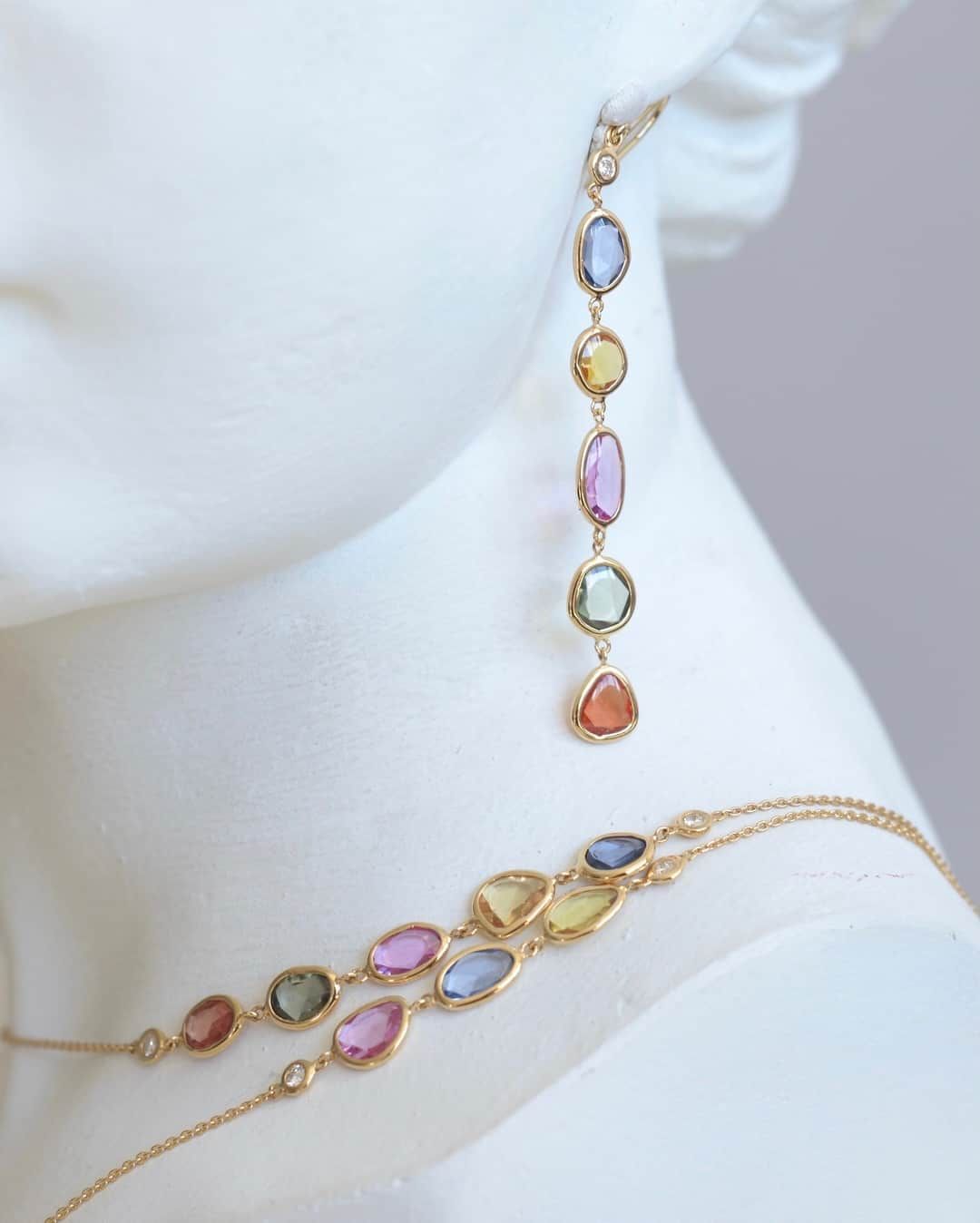 Bijoux en or, boucles d'oreilles et collier, avec pierres précieuses multicolores en forme de larme, présentés sur un buste blanc.