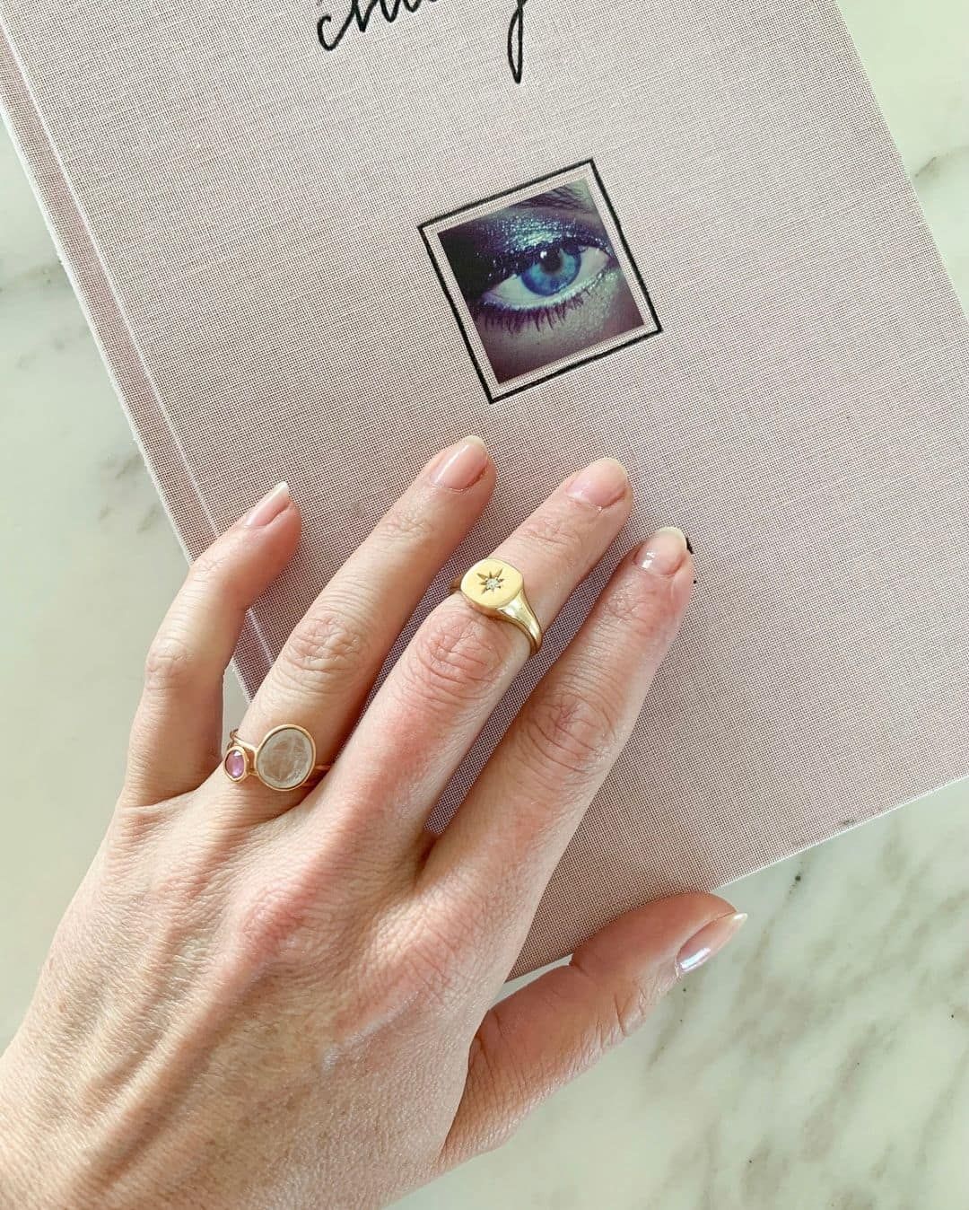 Une main portant des bagues repose sur un livre rose avec une image d'œil.