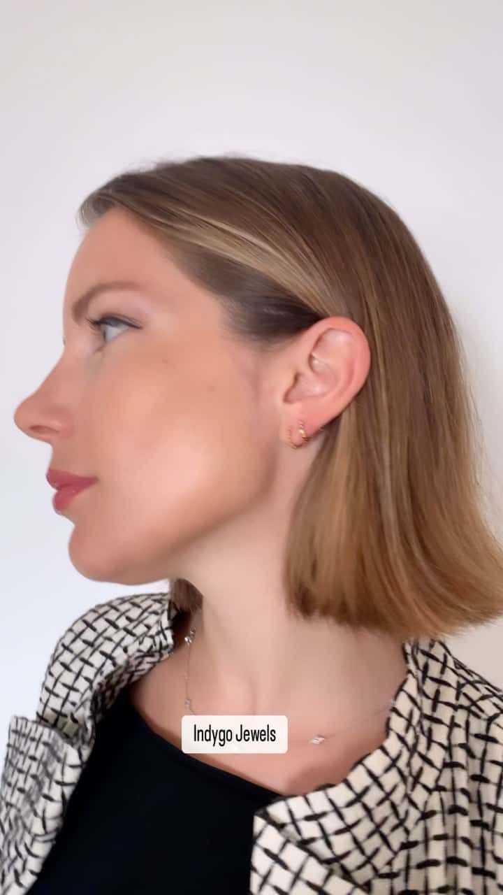 Femme aux cheveux blonds courts, de profil, portant de petites boucles d'oreilles et une veste à carreaux noirs et blancs.