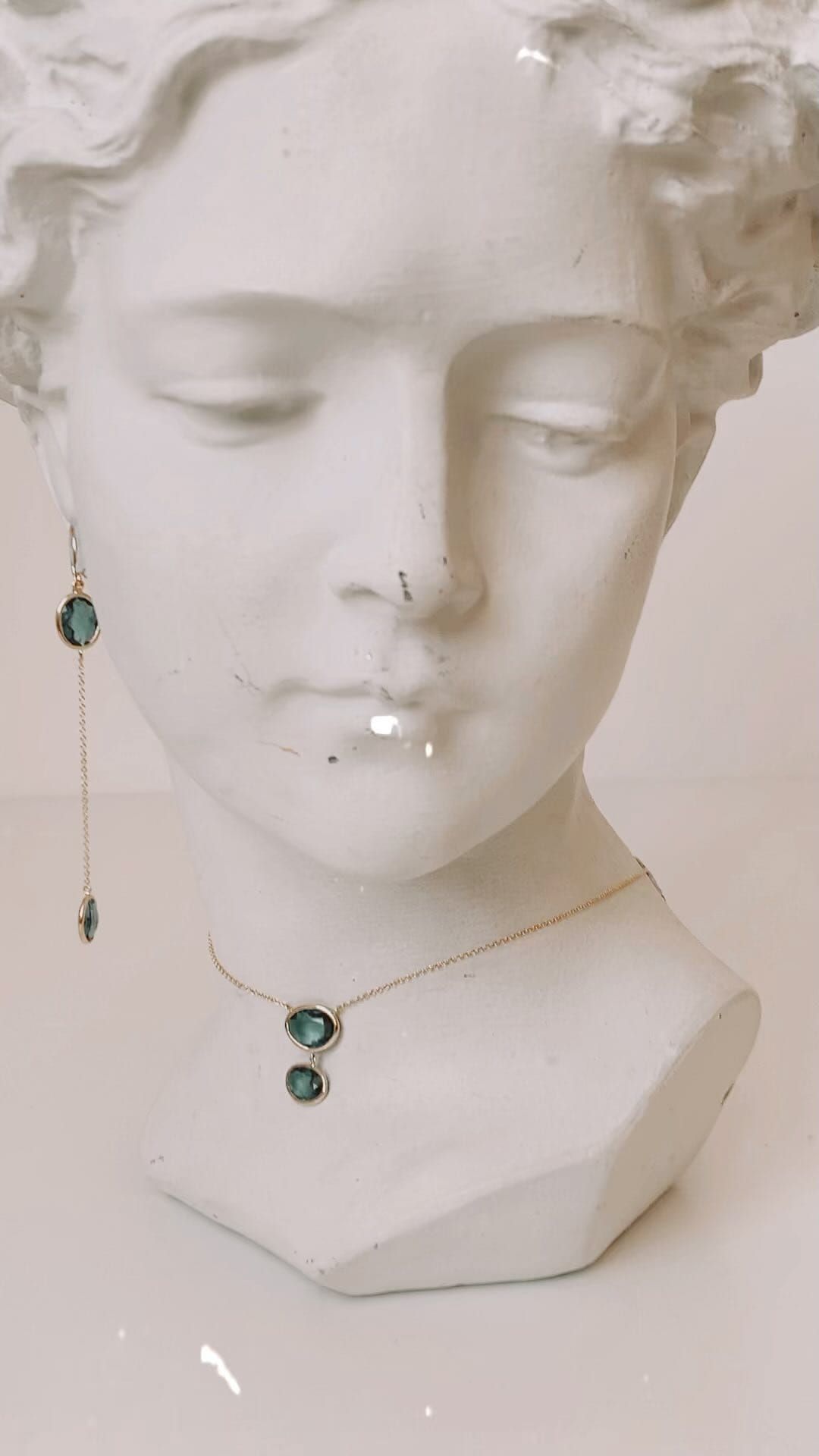 Buste en plâtre blanc portant un collier et une boucle d'oreille en pierres précieuses bleues.