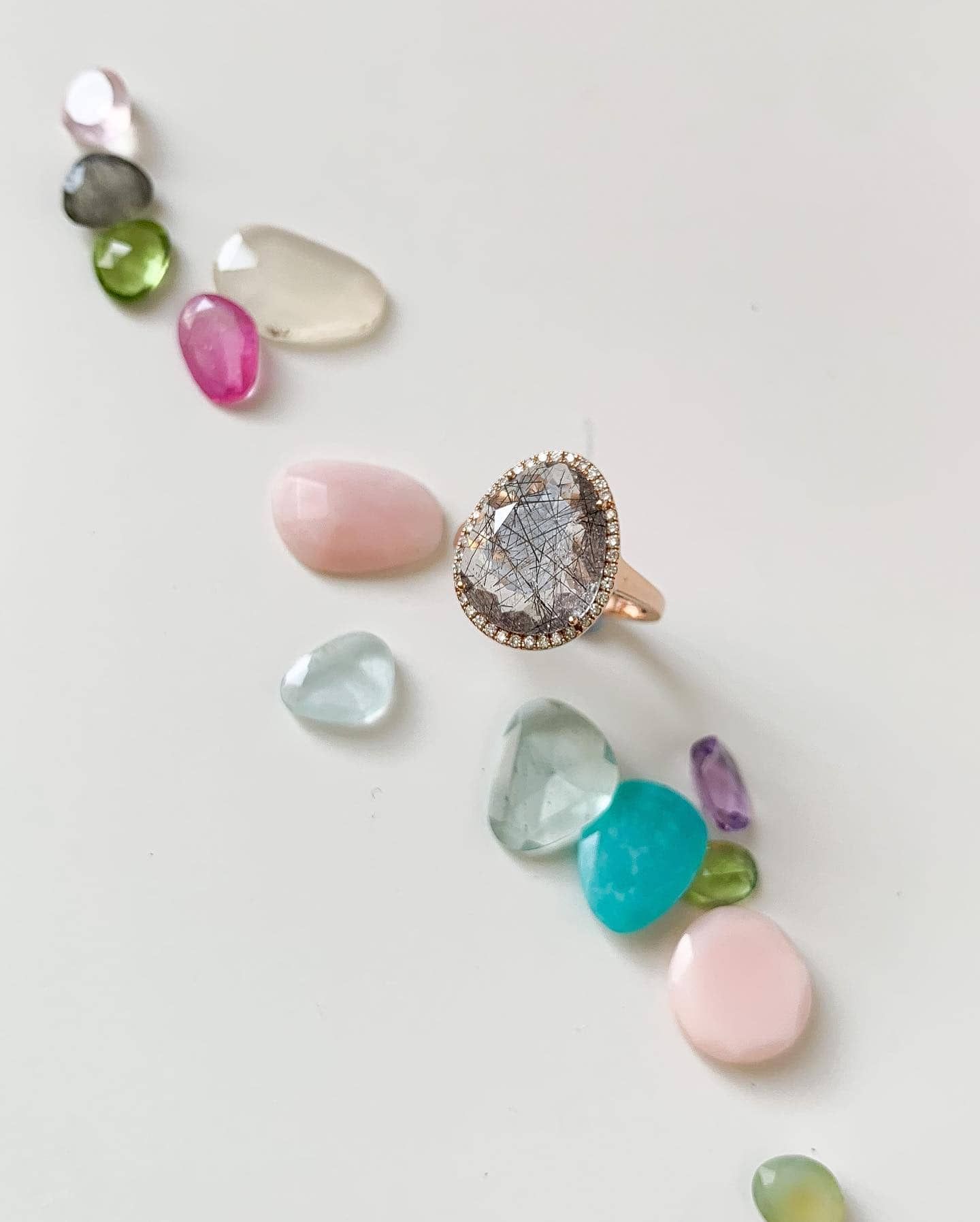 Bague en or avec une grosse pierre précieuse grise, entourée de pierres précieuses colorées dispersées.