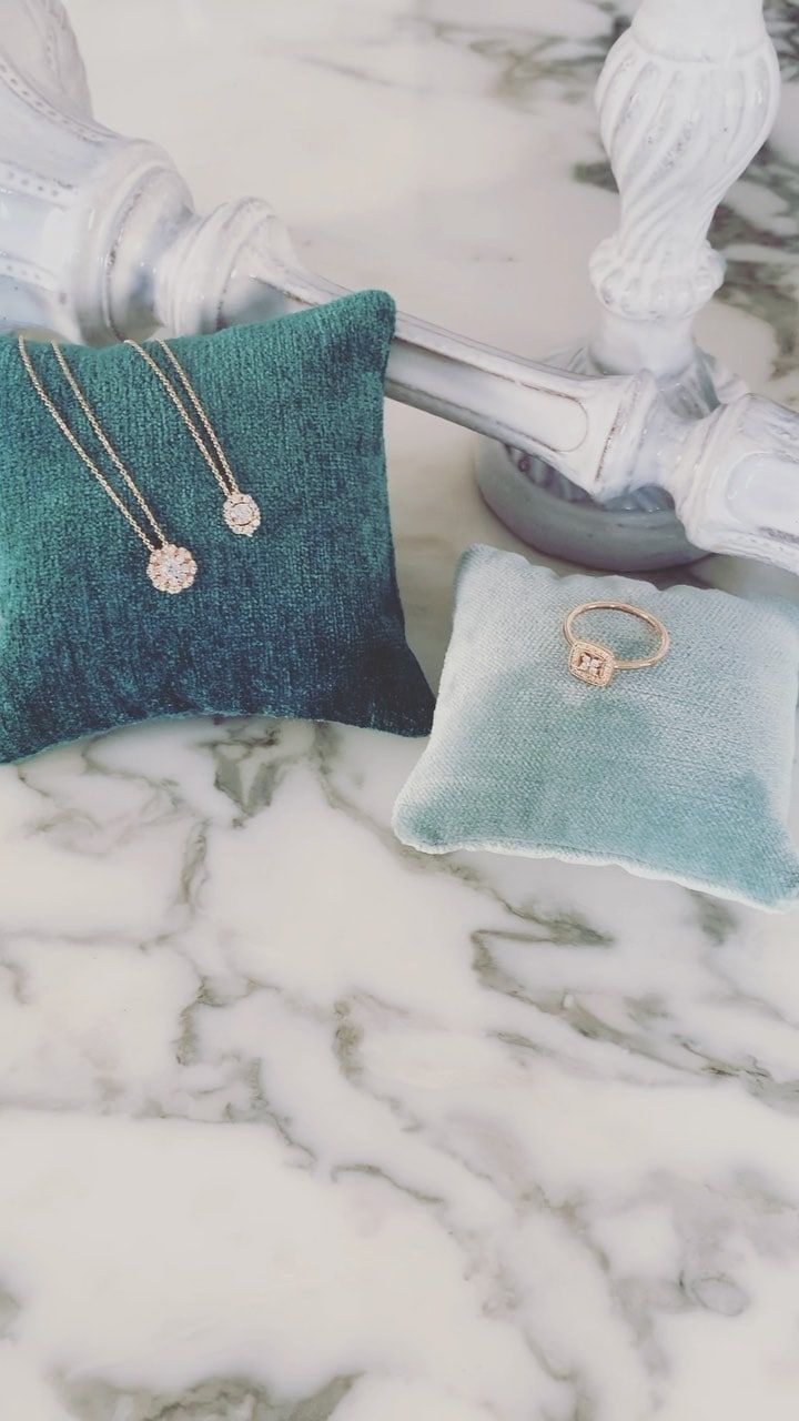 Bijoux présentés sur des coussins en velours bleu sarcelle sur un fond en marbre.
