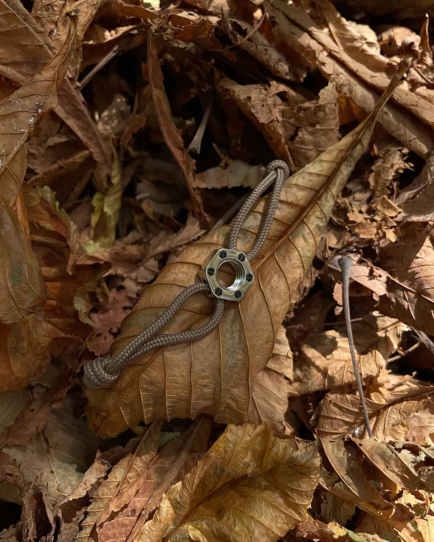 Bracelet au design circulaire central reposant sur une feuille tombée au milieu de feuilles d'automne tombées.