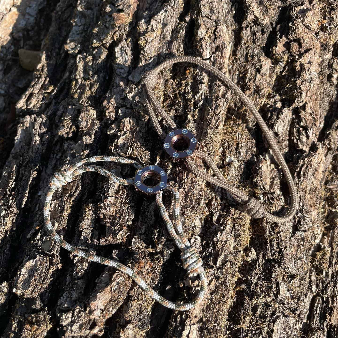 Deux bracelets en paracorde avec des accents en métal foncé reposant sur l'écorce d'un arbre.