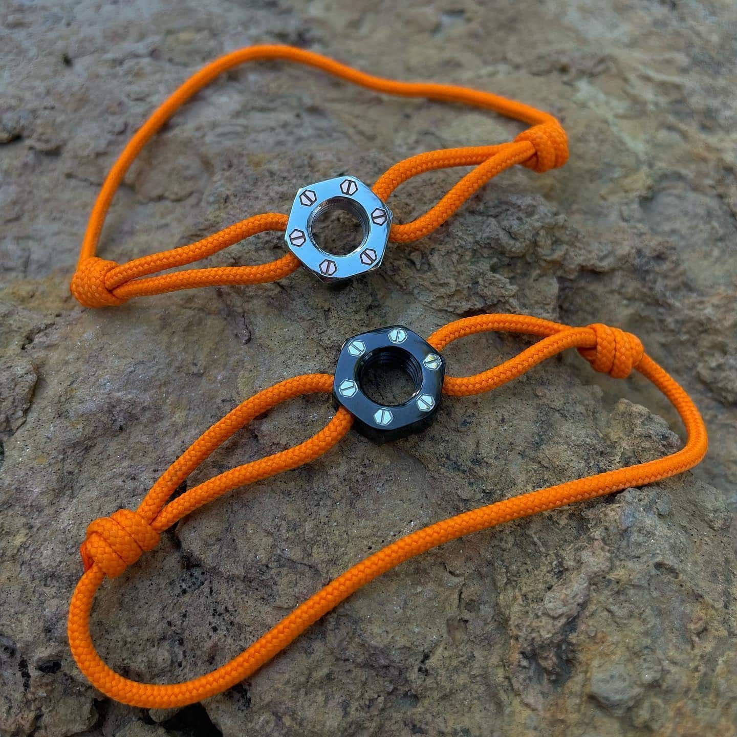 Deux bracelets en paracorde orange avec des perles hexagonales en métal sur un rocher.