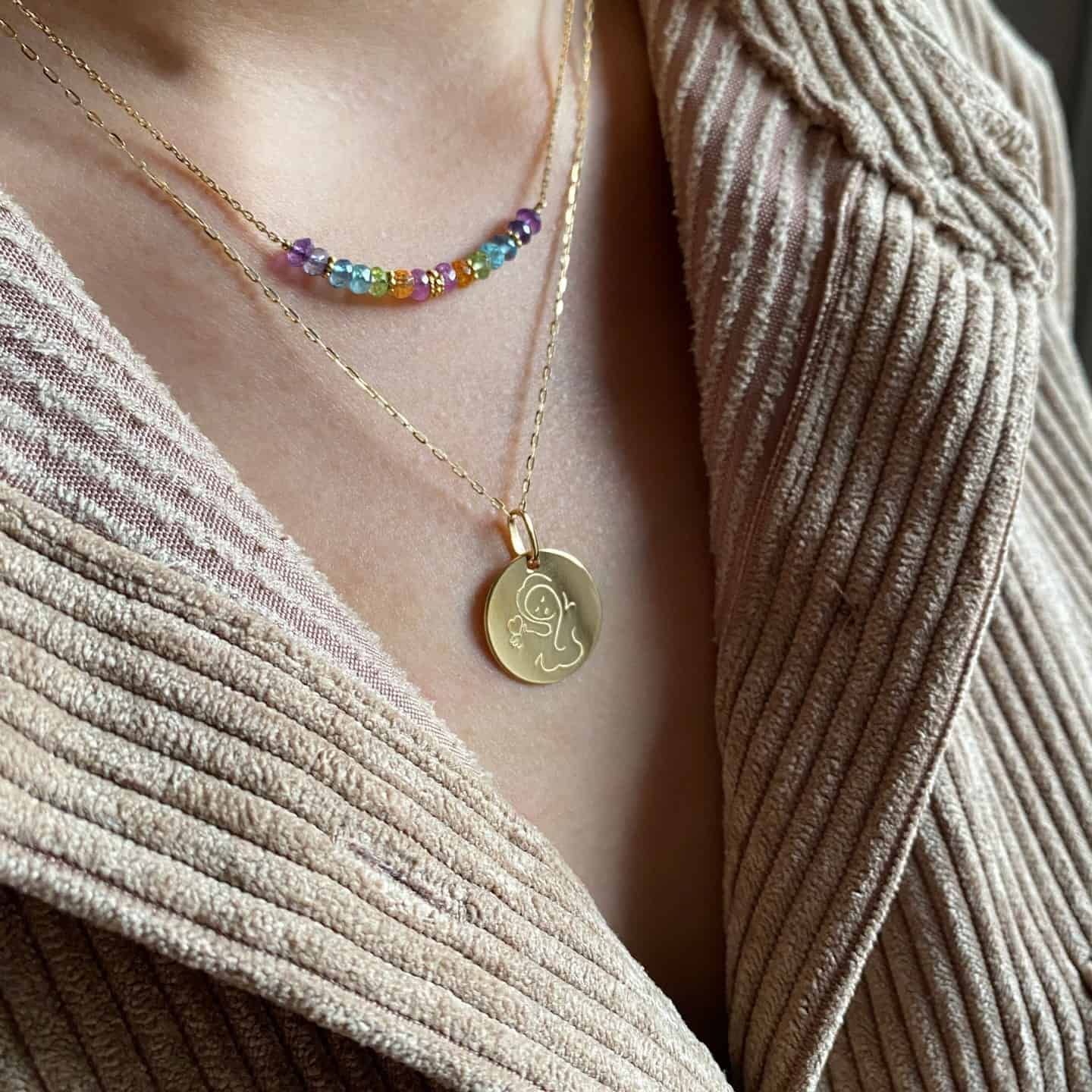 Femme portant trois colliers : un avec des perles colorées, deux colliers avec pendentifs en or.