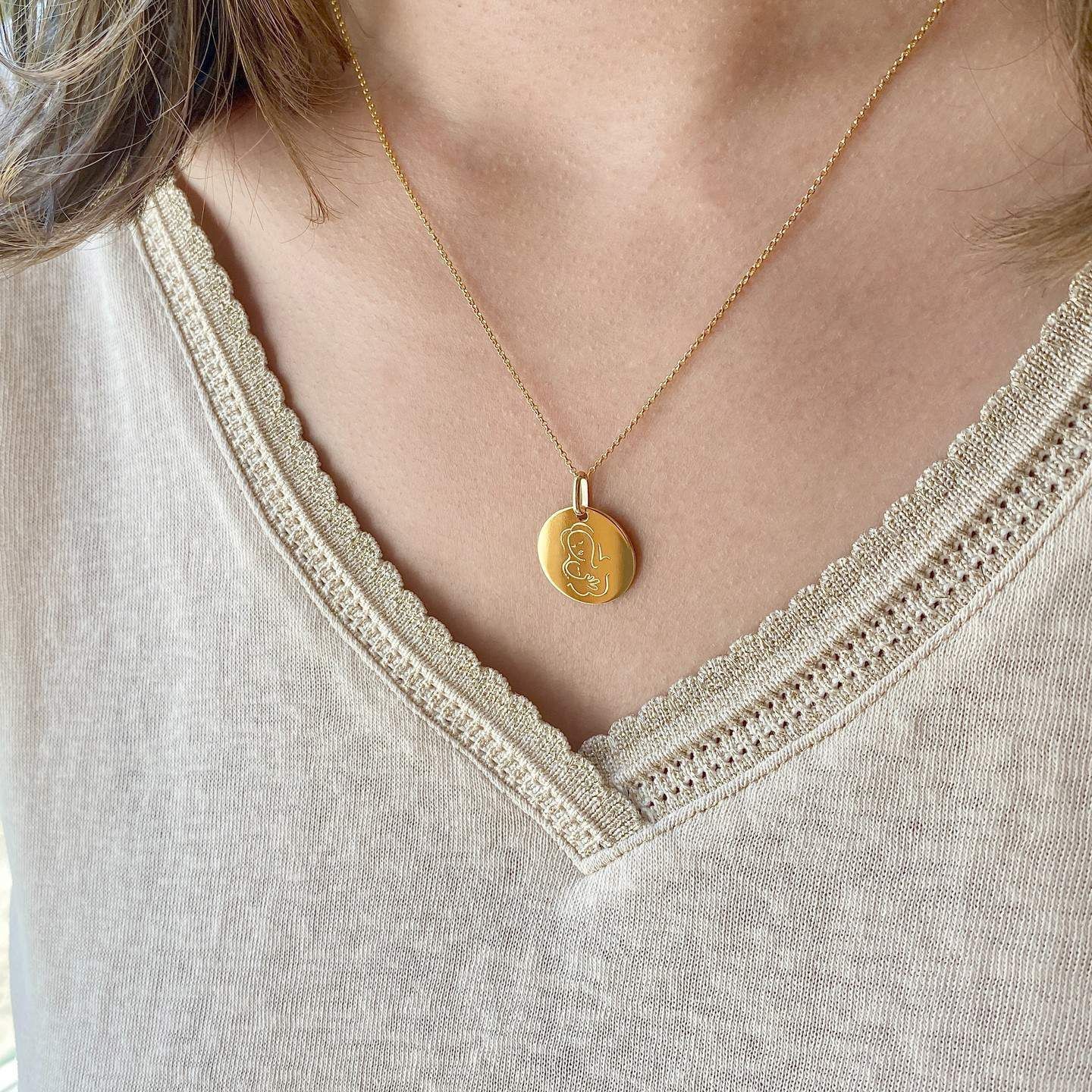 Femme portant un collier en or avec un pendentif et un haut beige.