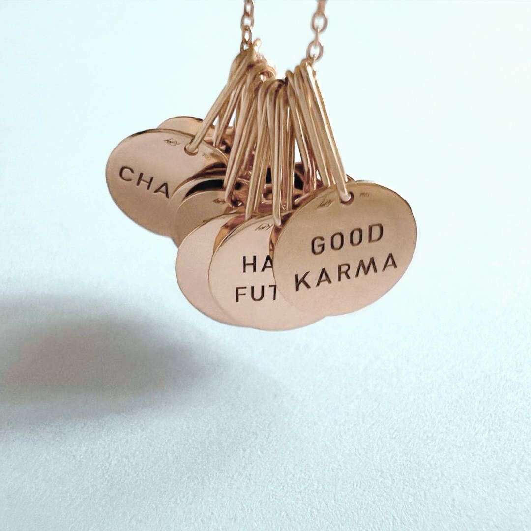 Collier en or rose avec breloques gravées sur lesquelles on peut lire « Bon Karma » et d'autres mots édifiants.