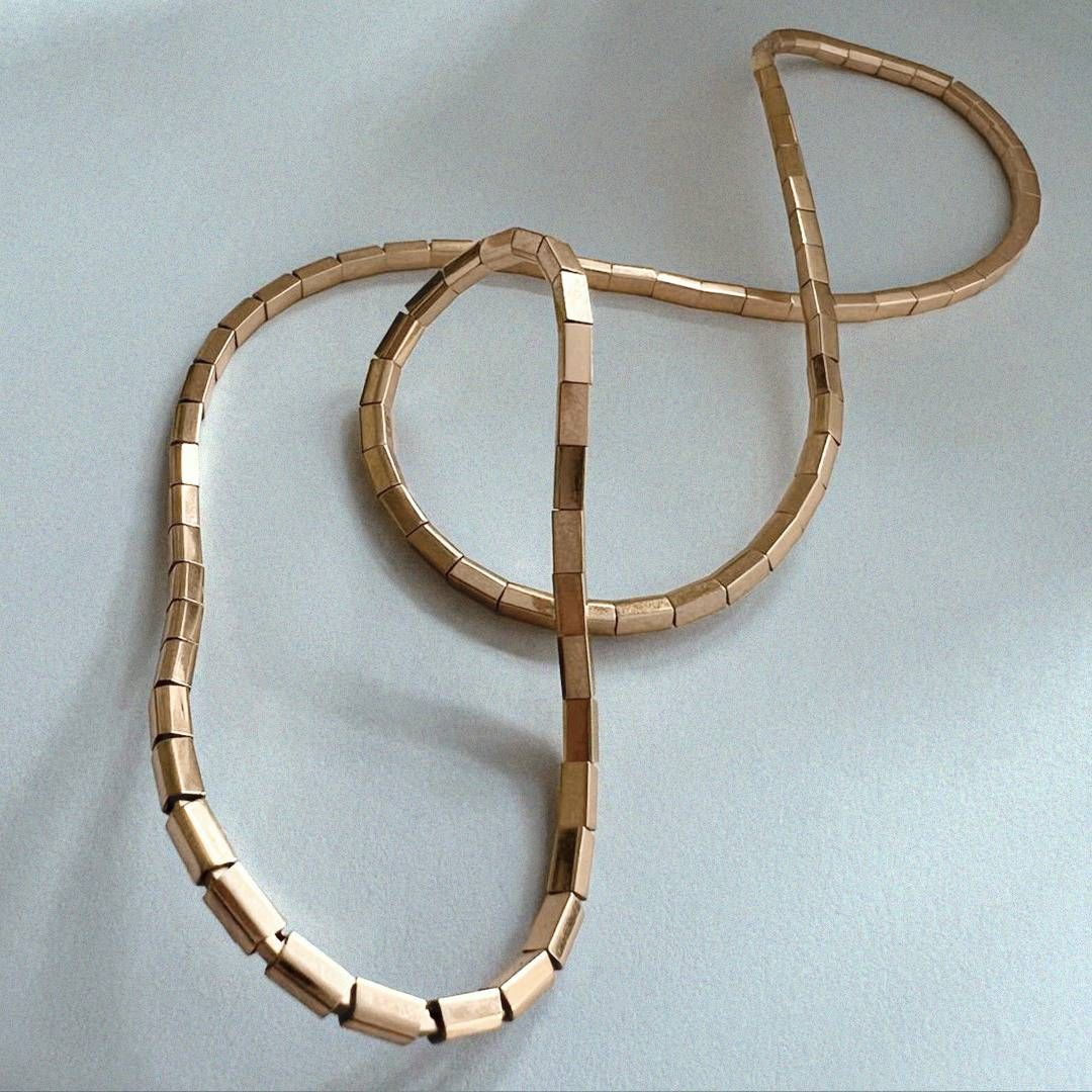 Collier à maillons rectangulaires dorés en forme de huit sur une surface blanche.