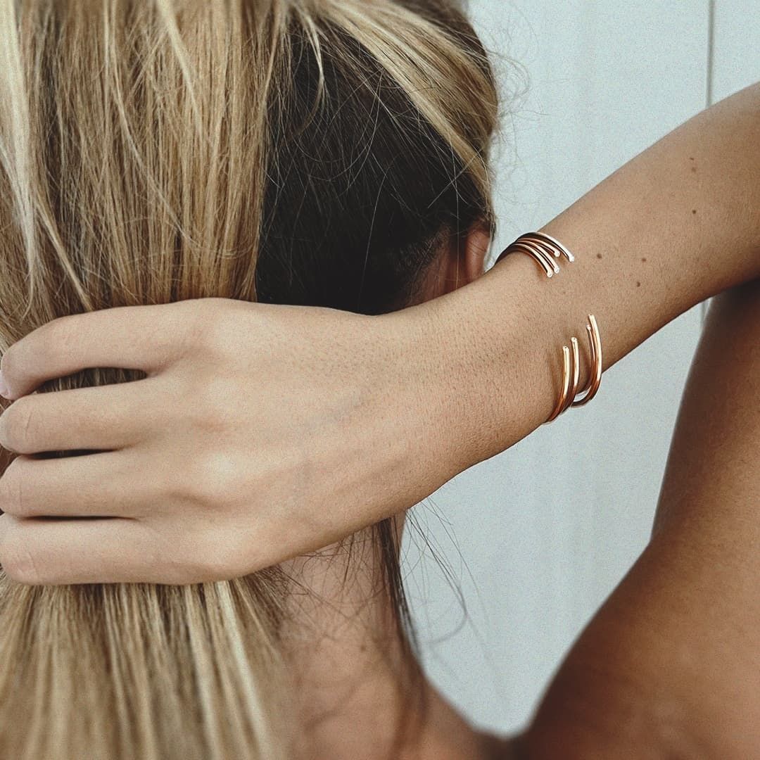 Femme aux cheveux blonds tirés en arrière, portant un bracelet manchette ouvert en or.