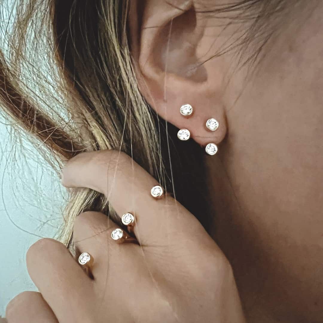 Oreille et main de femme ornées de plusieurs petites boucles d'oreilles scintillantes en formation de grappe.