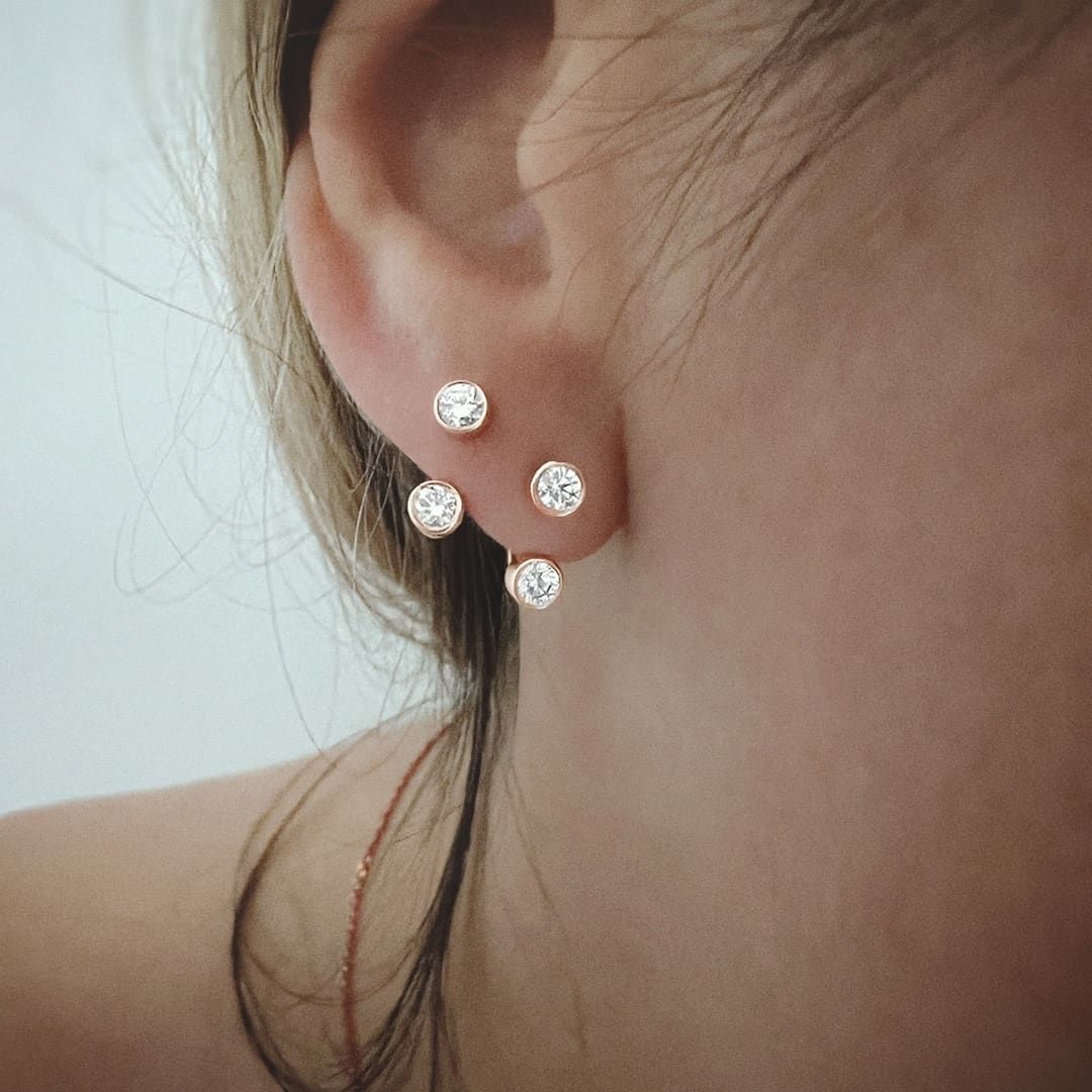 Gros plan d'une oreille ornée de quatre clous d'oreilles en diamant. La peau est claire et le décor est intérieur.