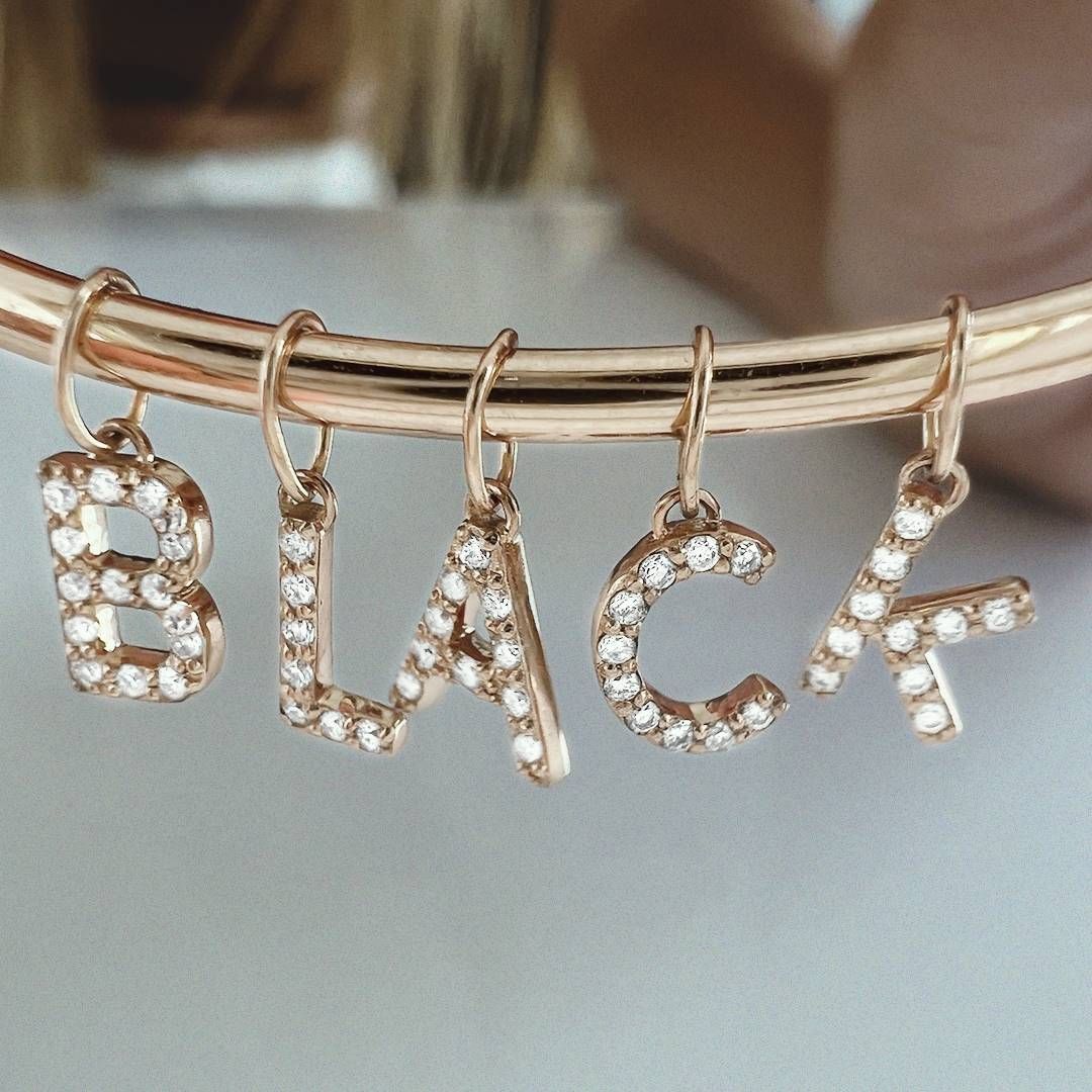 Bracelet en or rose avec breloques scintillantes en forme de lettre orthographiée « BLACK ».