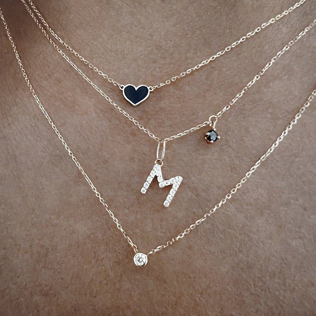 Trois colliers en or avec pendentifs : un cœur, une lettre « M » et un seul diamant.