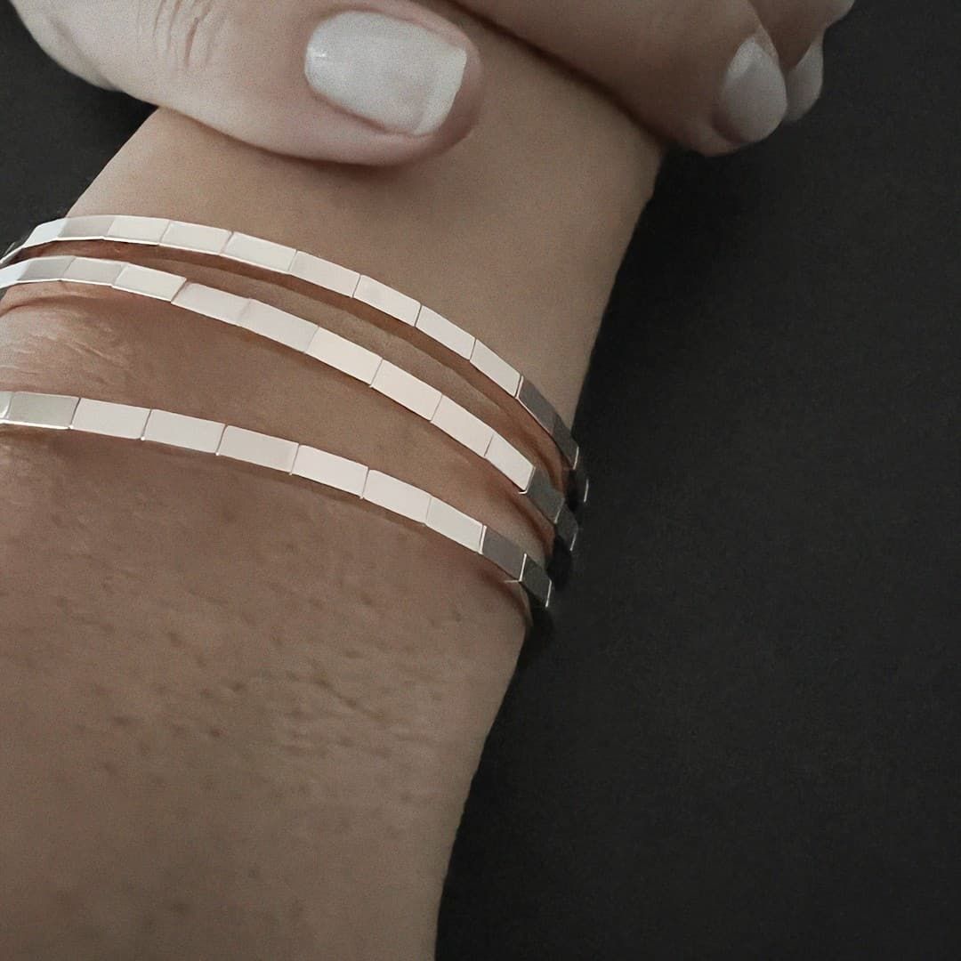 Poignet d'une personne avec trois bracelets fins en or rose. Main encadrée avec vernis à ongles clair.