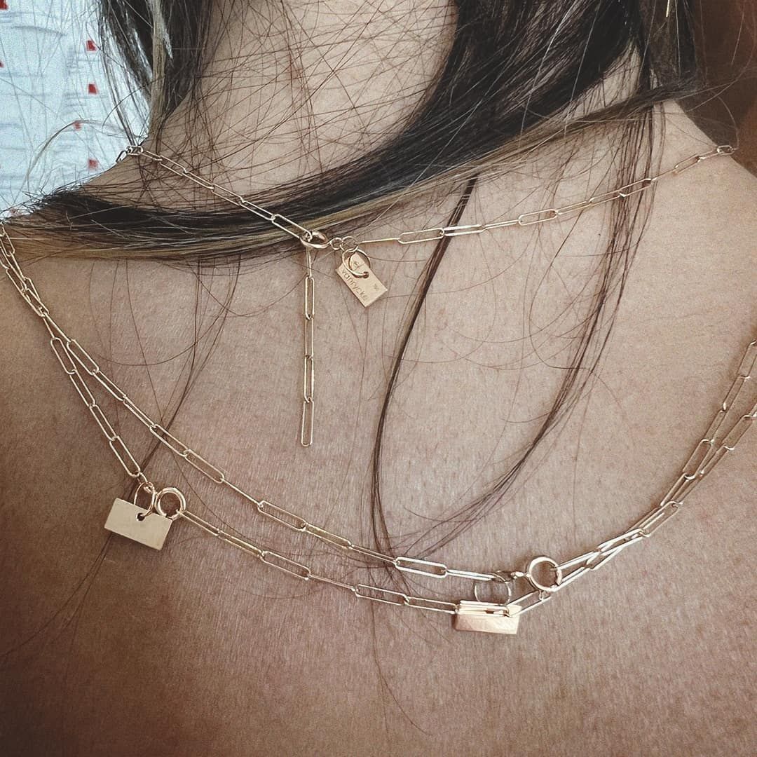 Gros plan du dos d'une personne portant des colliers en or superposés, notamment des chaînes délicates avec des pendentifs et de petits cadenas.