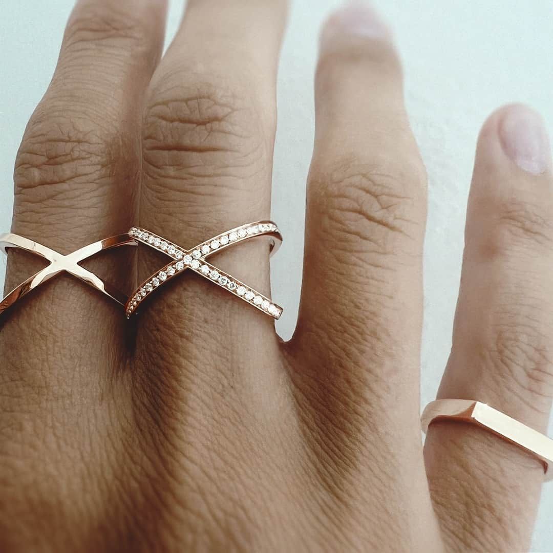 Main portant trois bagues en or rose, deux modèles croisés et une bande simple.