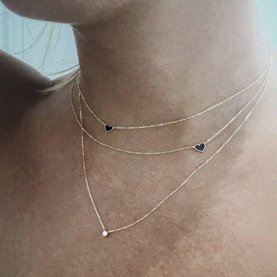 Trois colliers en or avec de petits pendentifs en forme de cœur et de diamant sur le cou d'une personne.