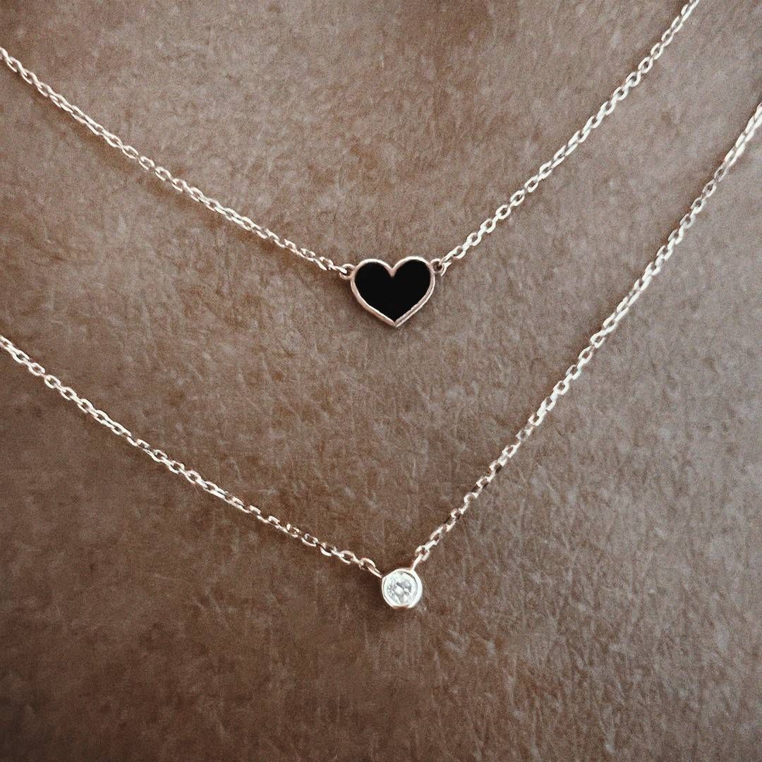 Deux colliers en or superposés, l'un avec un pendentif en forme de cœur noir, l'autre avec un diamant.